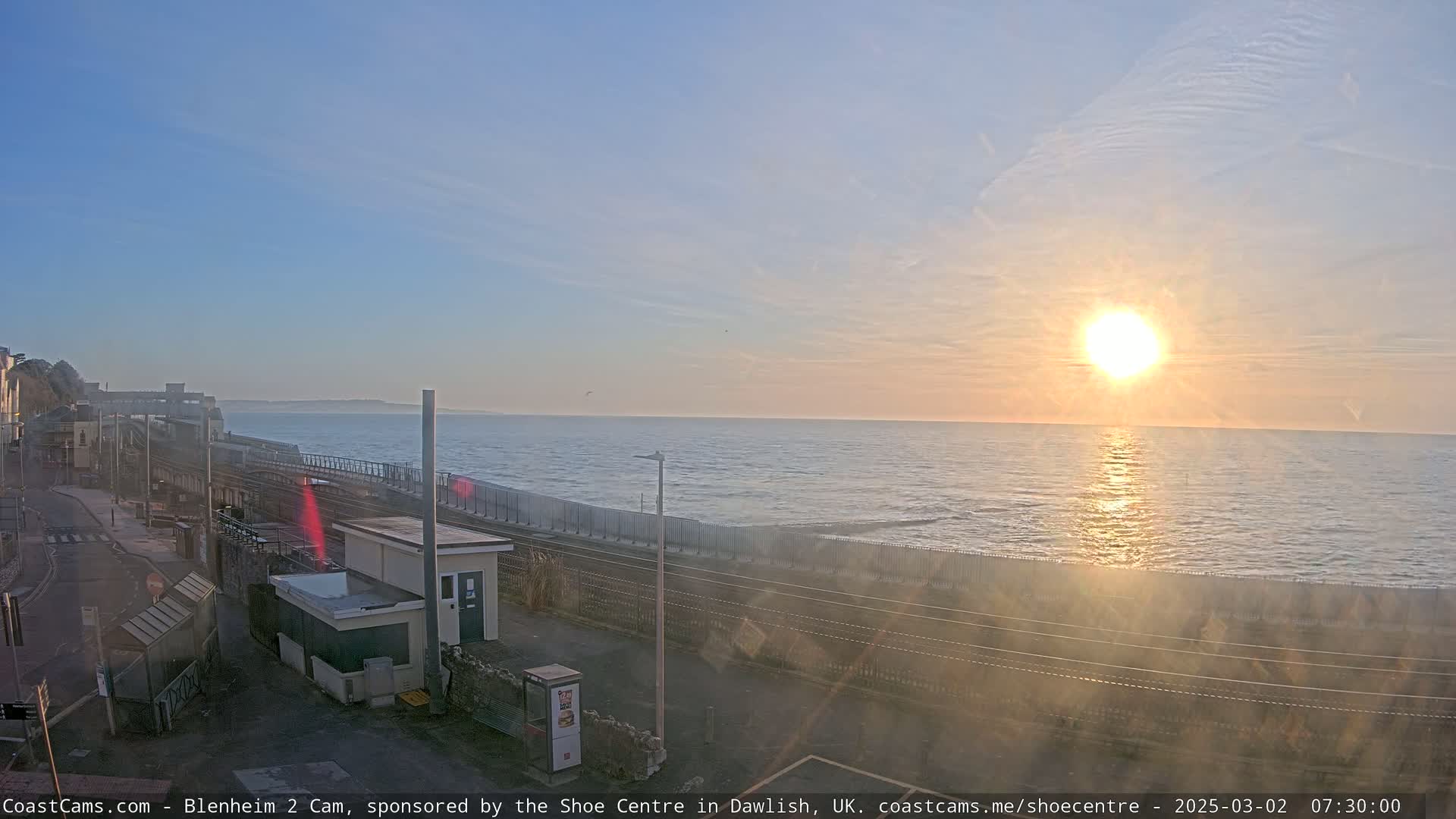 A sunrise over a calm ocean, viewed from a coastal train station.