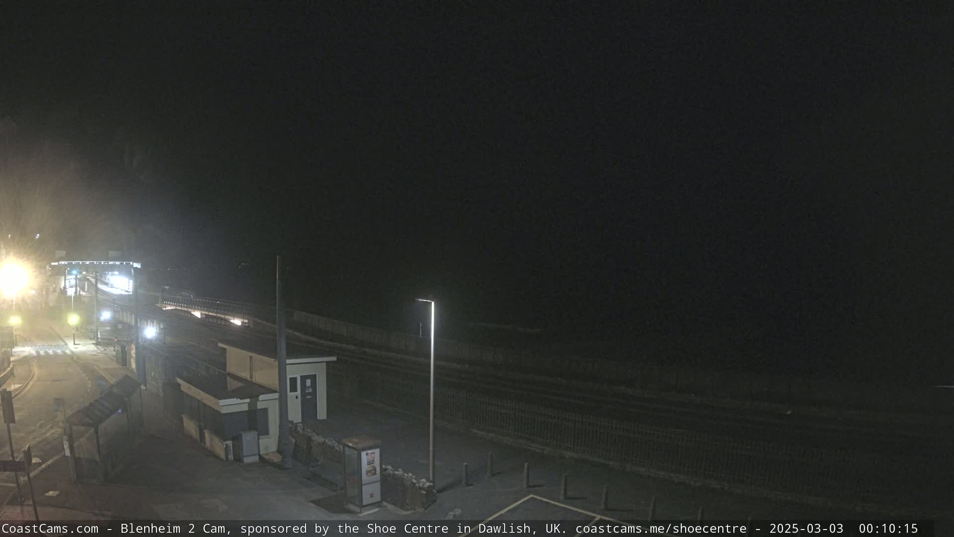 A nighttime view of a mostly empty train station platform next to a dark ocean under a clear sky.