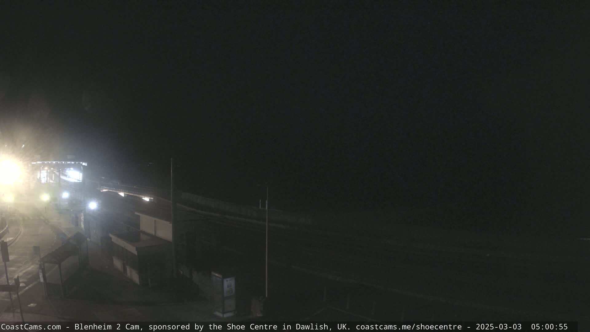 A nighttime, dimly lit coastal road scene with a dark ocean in the background.