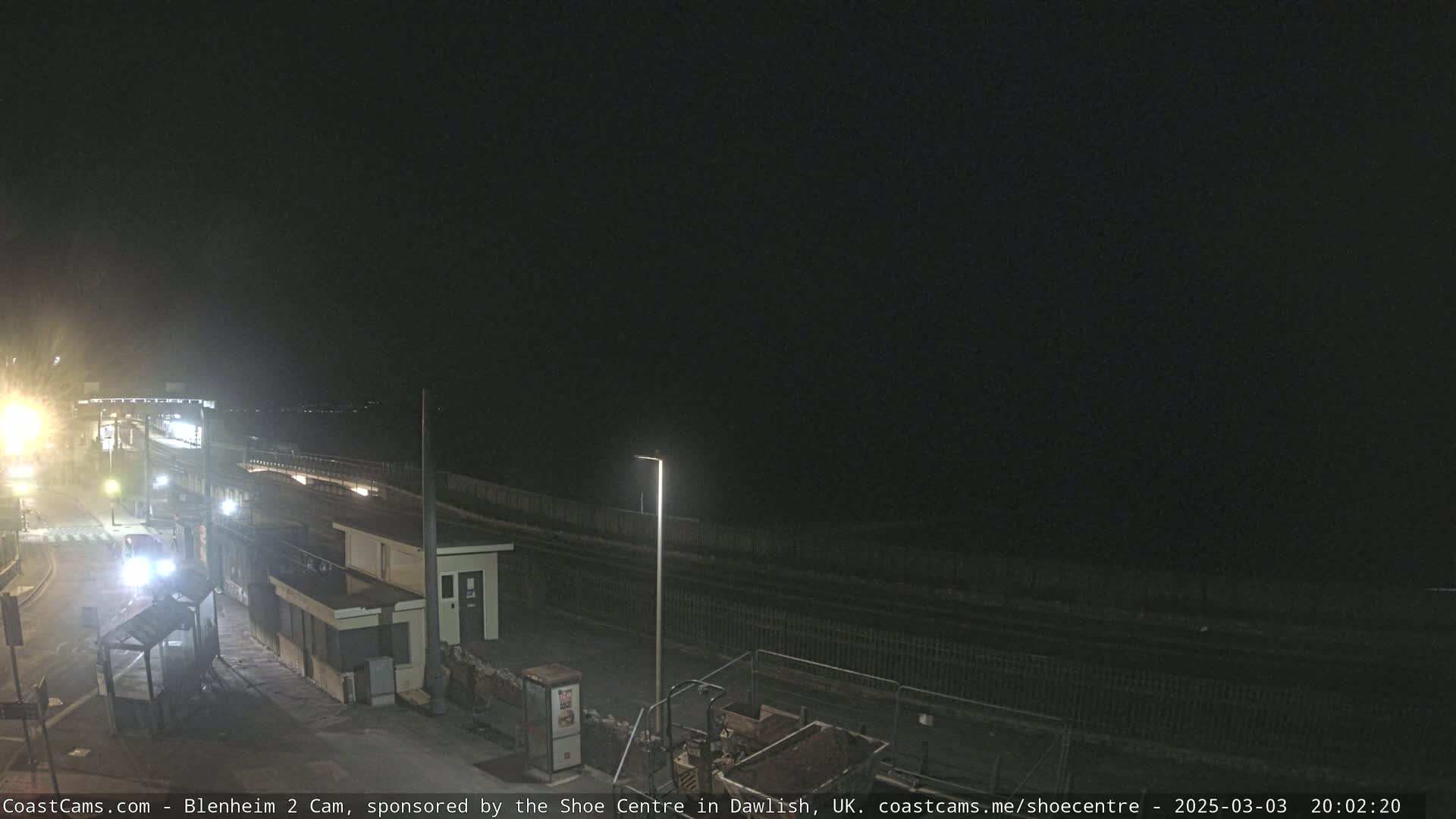 A nighttime view of a train station platform and surrounding area under a dark sky.