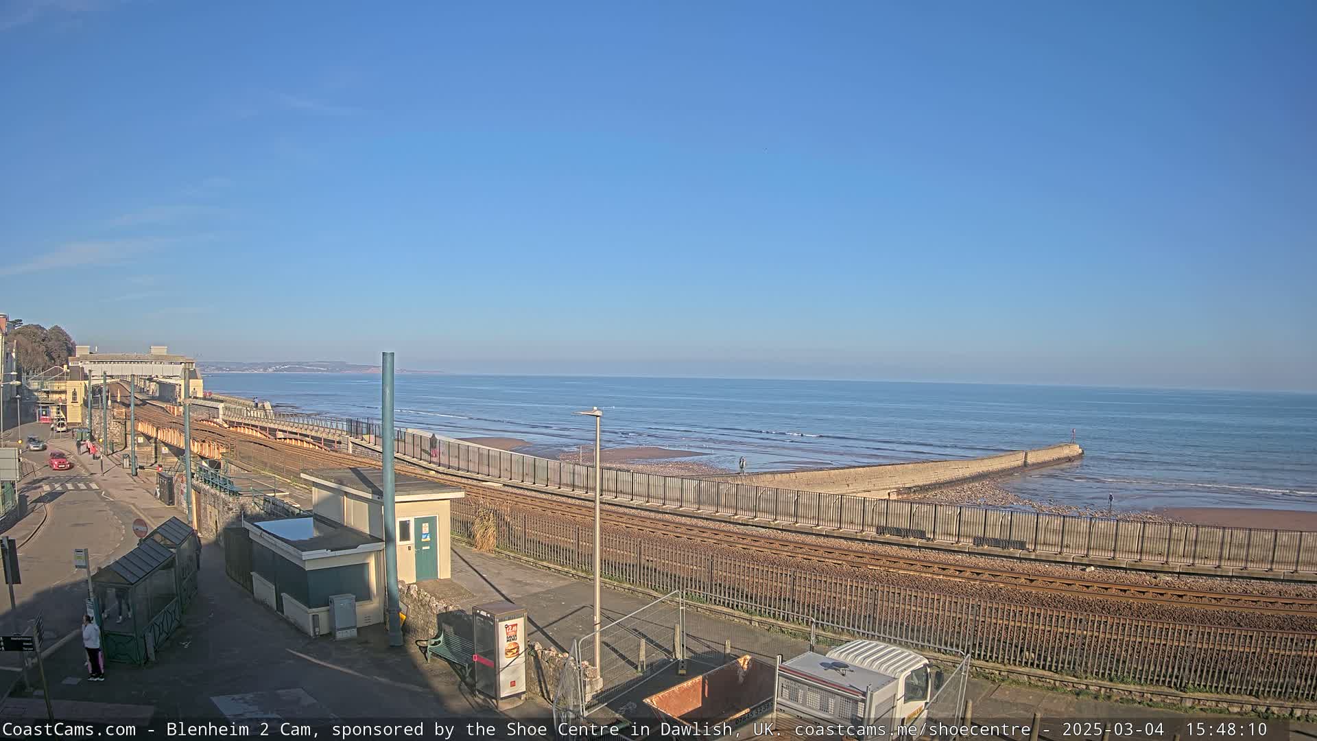 A seaside town with train tracks running alongside a beach, under a clear blue sky.