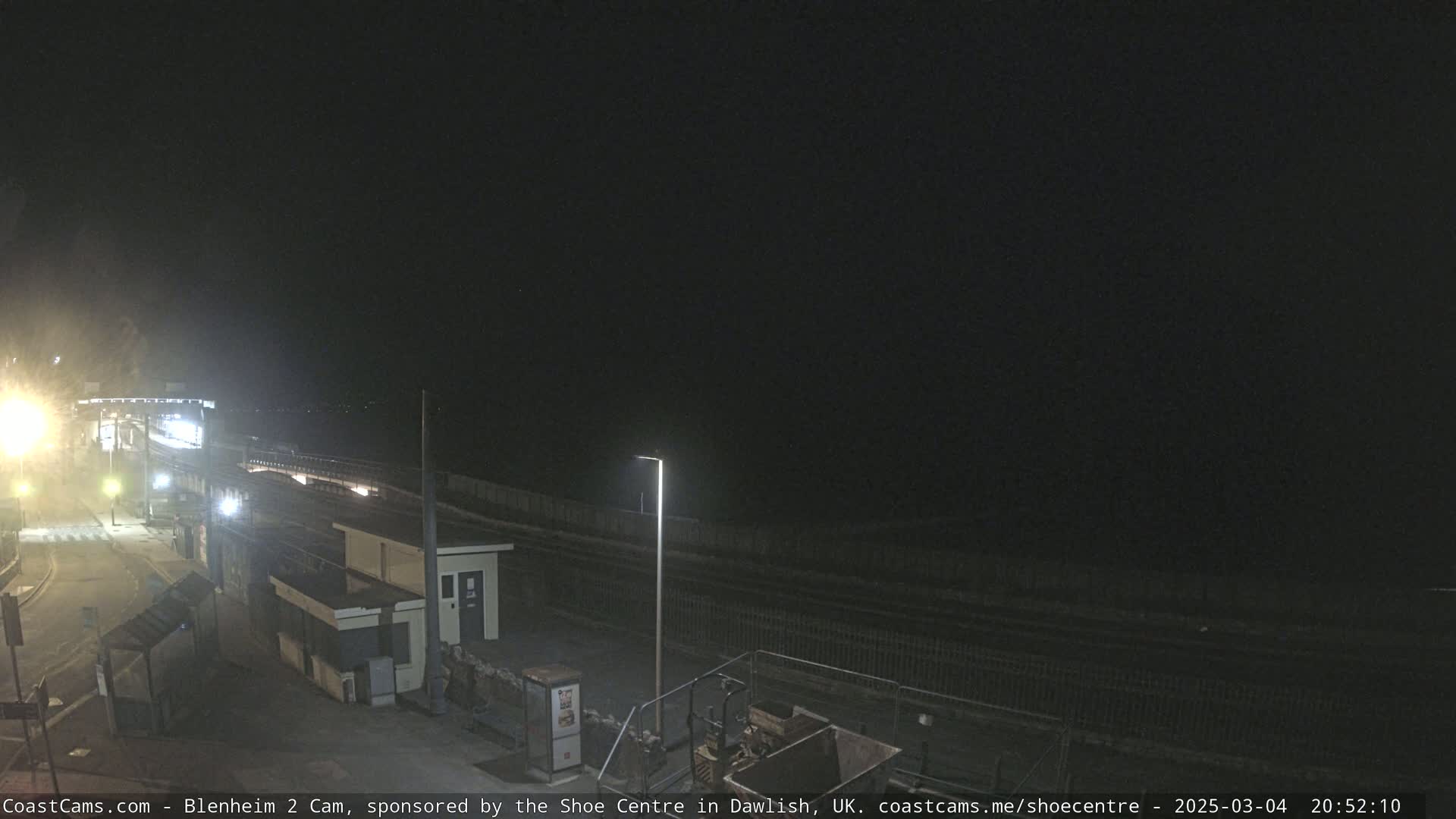 A nighttime view of a train station platform and surrounding area, under a dark, clear sky.