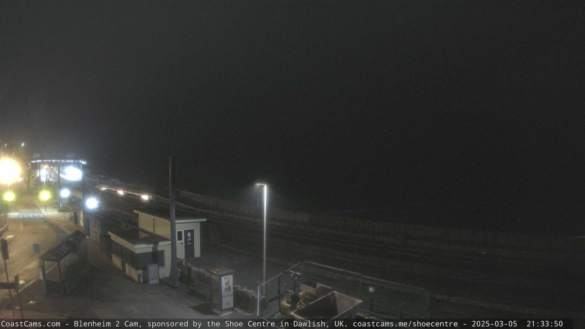 A nighttime, foggy view of a train station platform with lights illuminating the area.