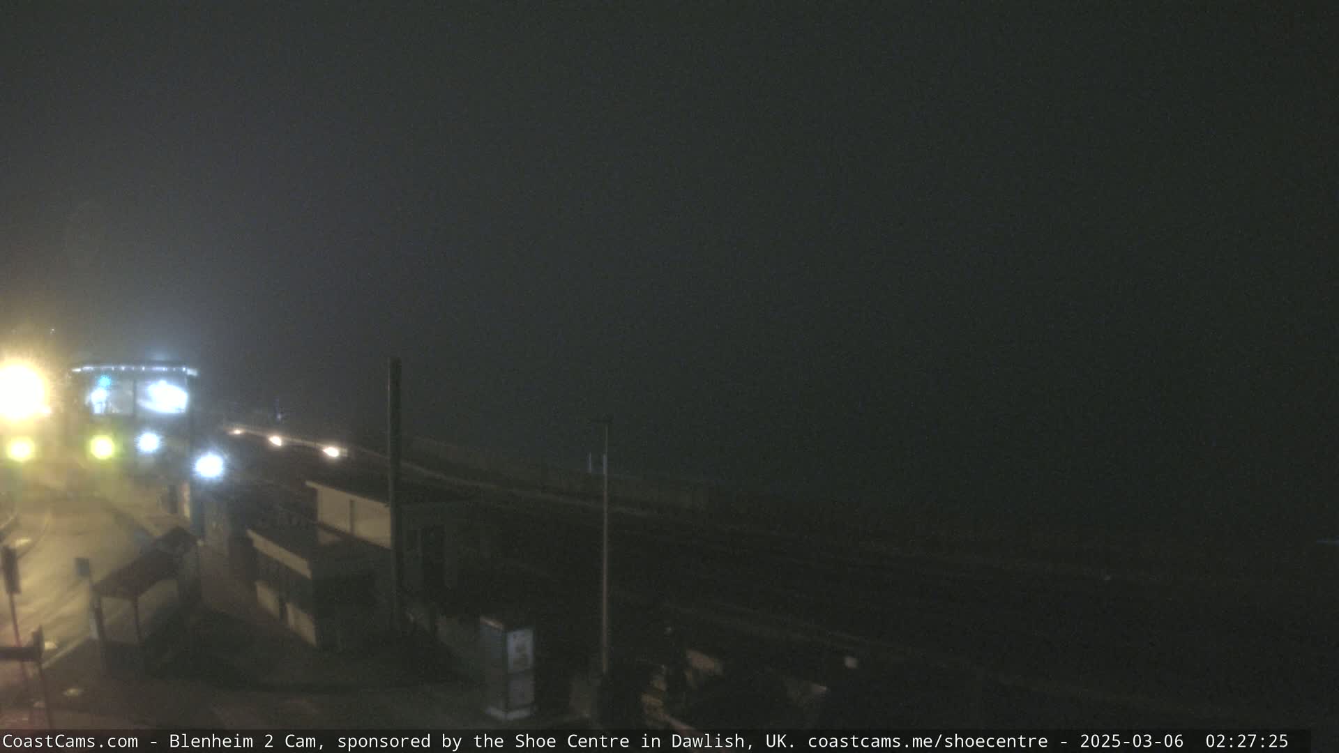 A foggy night scene shows a road with lights and buildings partially obscured by darkness and heavy fog.