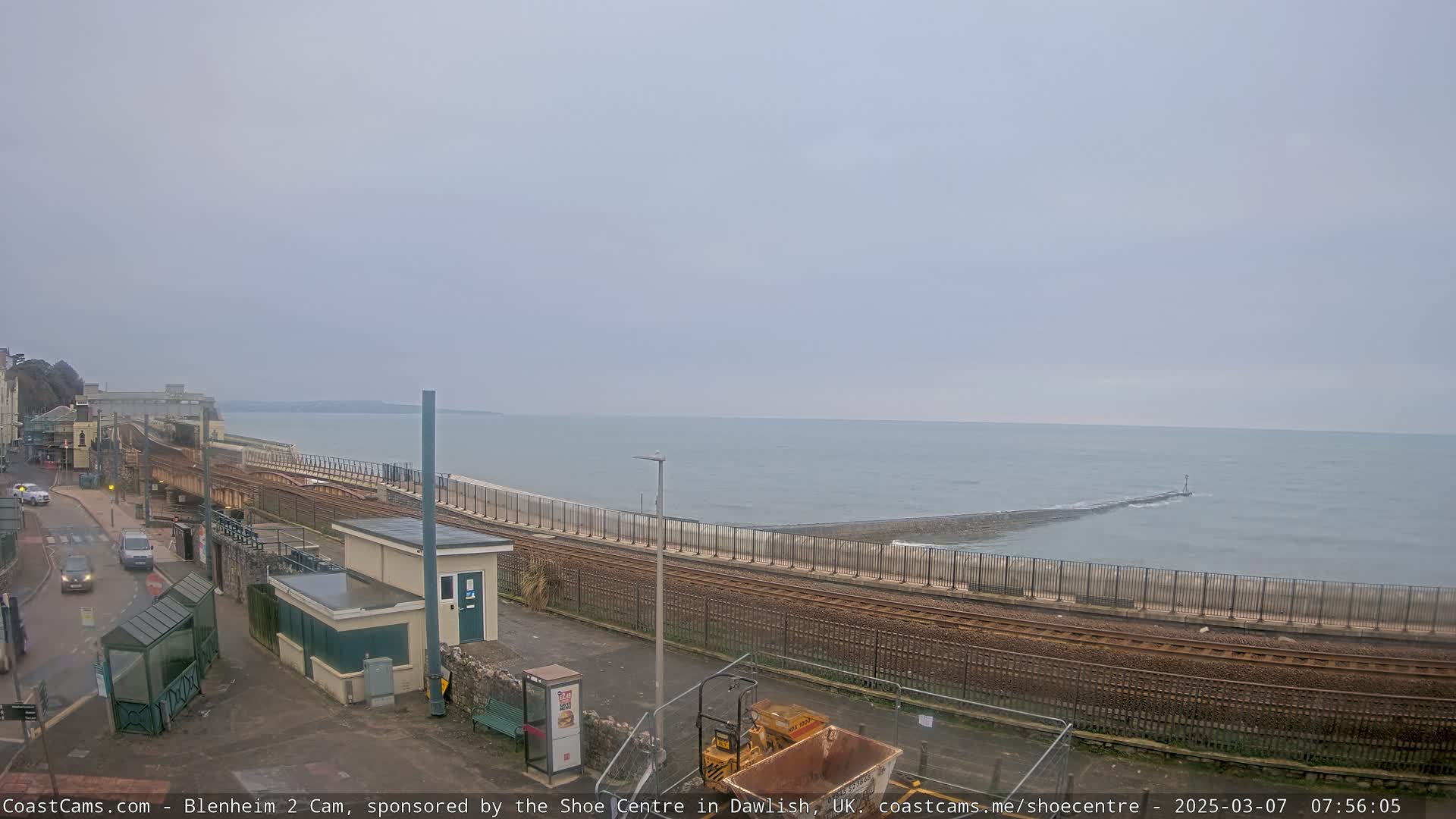 A coastal railway line runs alongside a calm, gray sea under an overcast sky.