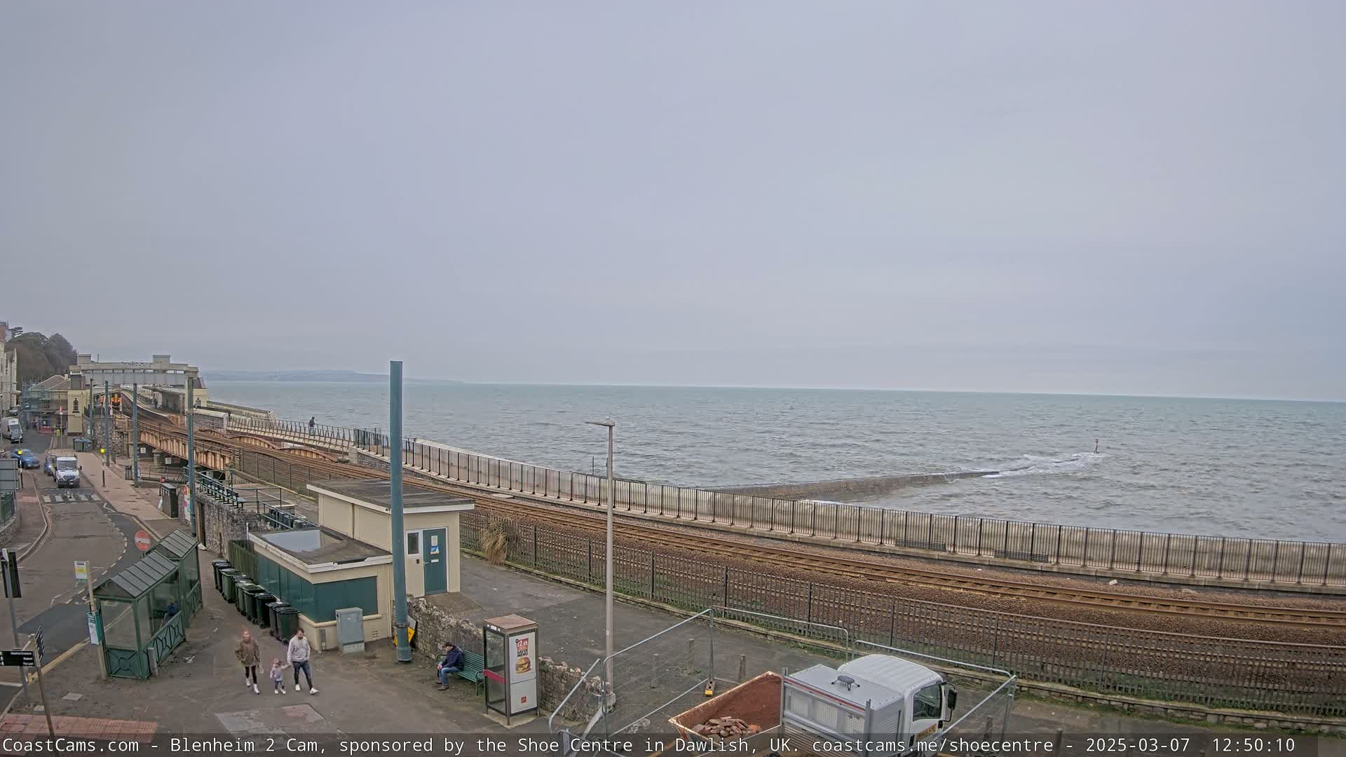 A coastal train track runs alongside a sea wall next to a choppy sea under an overcast sky.