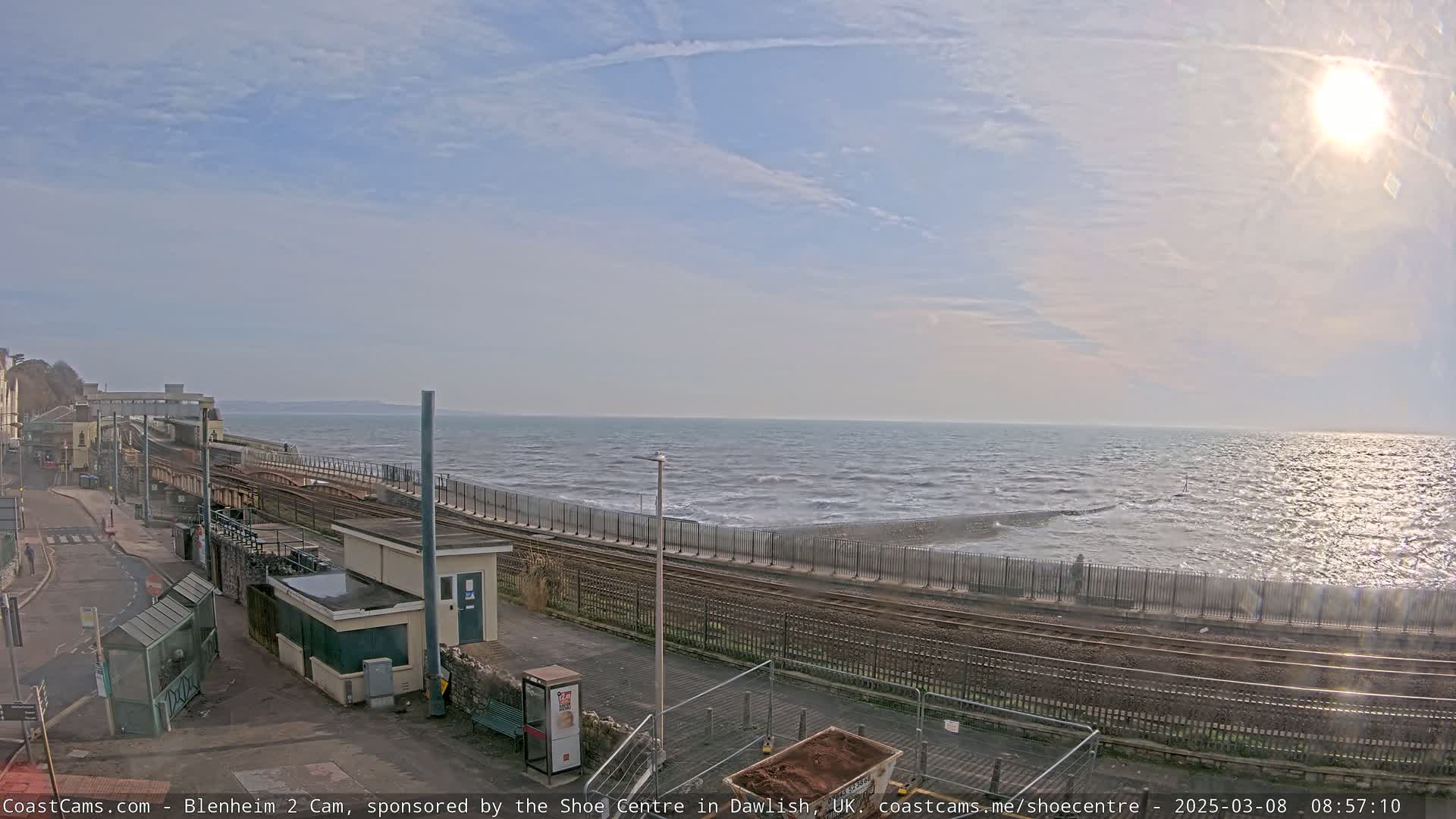 A sunny day at a seaside train station with choppy waves crashing against a seawall.