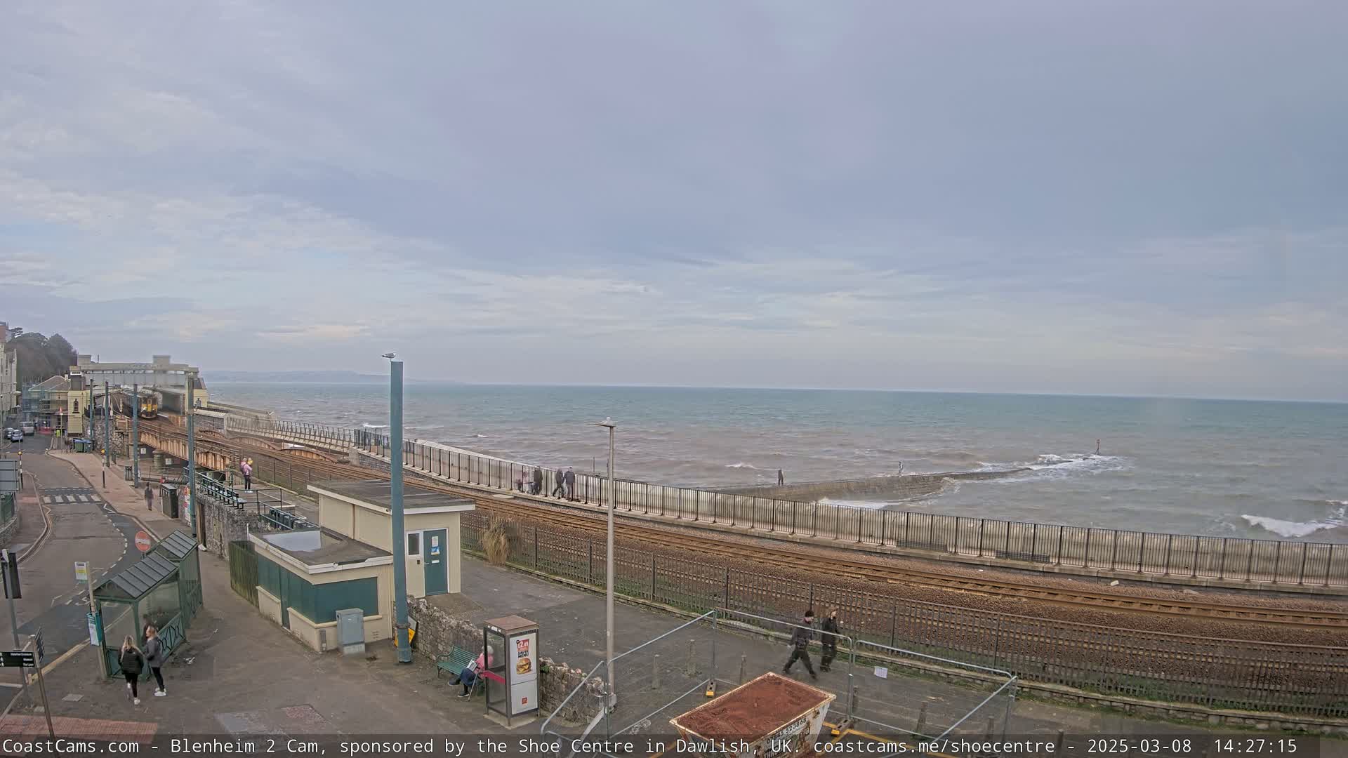 A train track runs alongside a coastline with a somewhat choppy sea under an overcast sky.