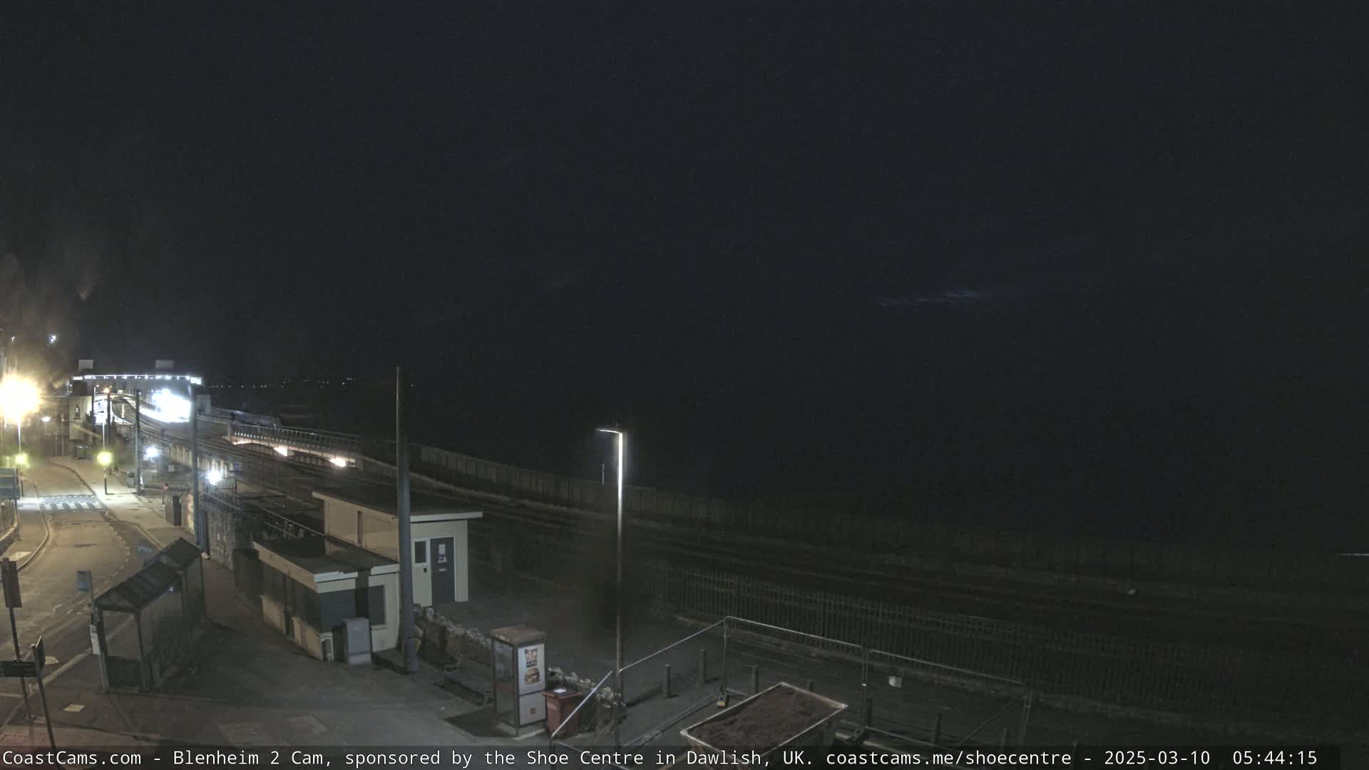 A nighttime view of a train station near a body of water under a dark sky.
