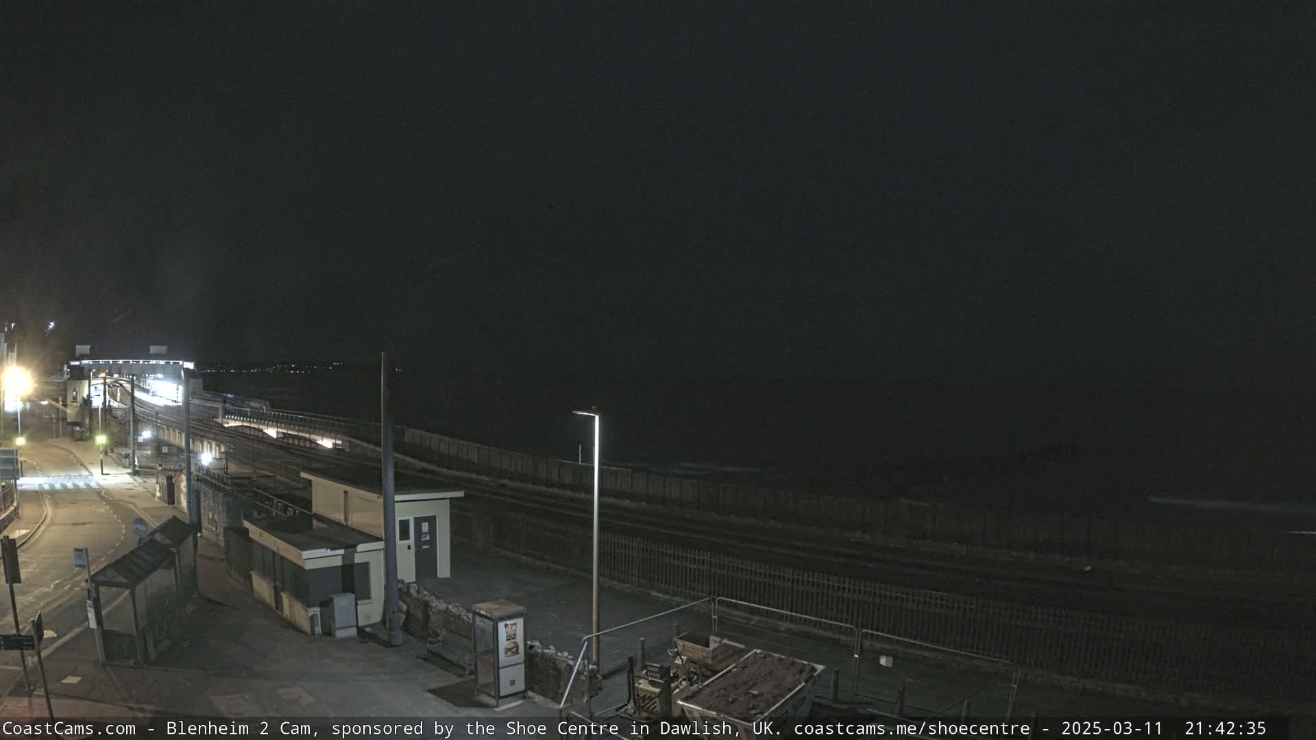 A nighttime view of a train station platform next to a body of water under a dark sky.