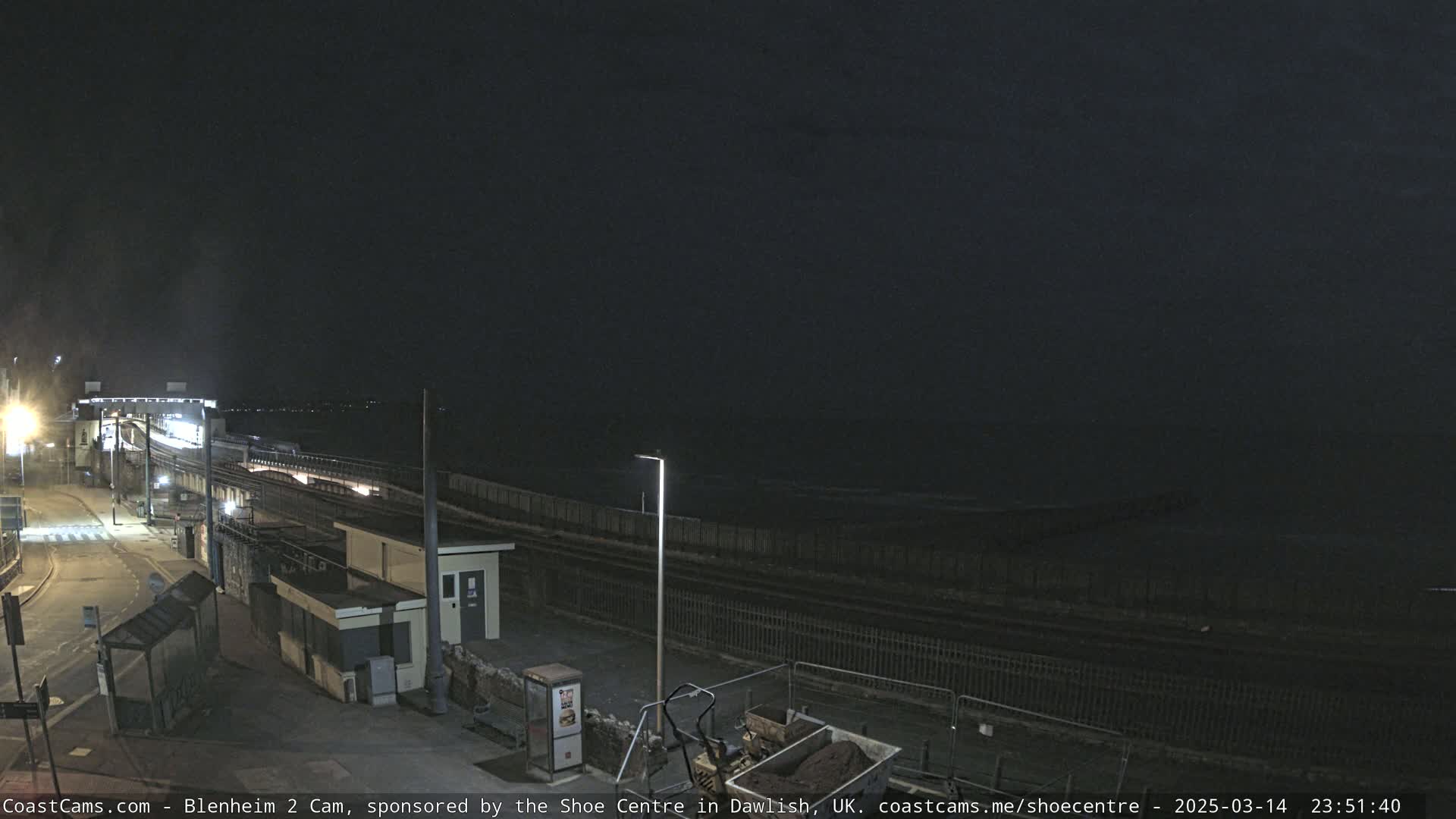 A nighttime view of a train station near a dark ocean under a mostly clear sky.