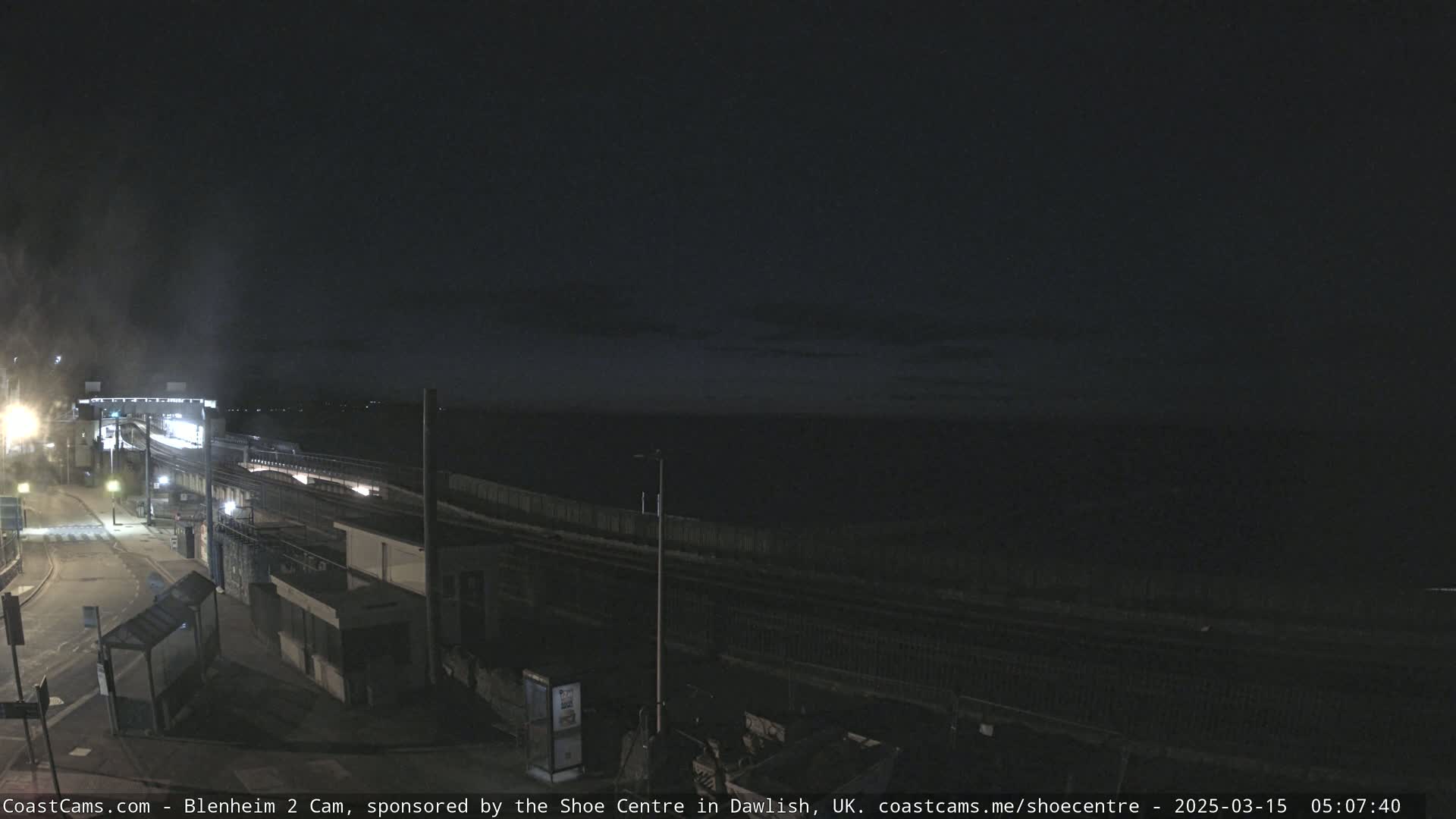A nighttime view of a train station near a dark body of water under a mostly clear sky.
