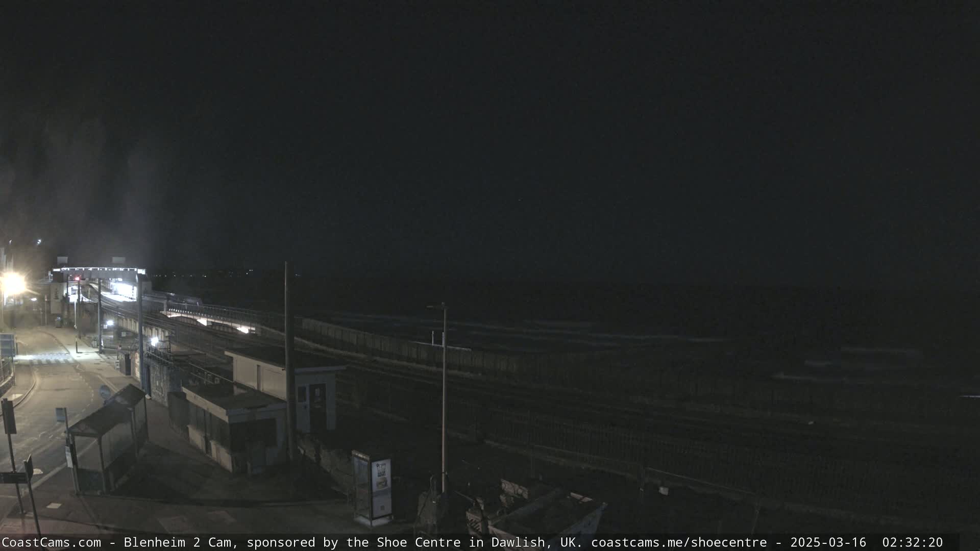 A nighttime view of a train station near a dark, wavy ocean under a clear, dark sky.
