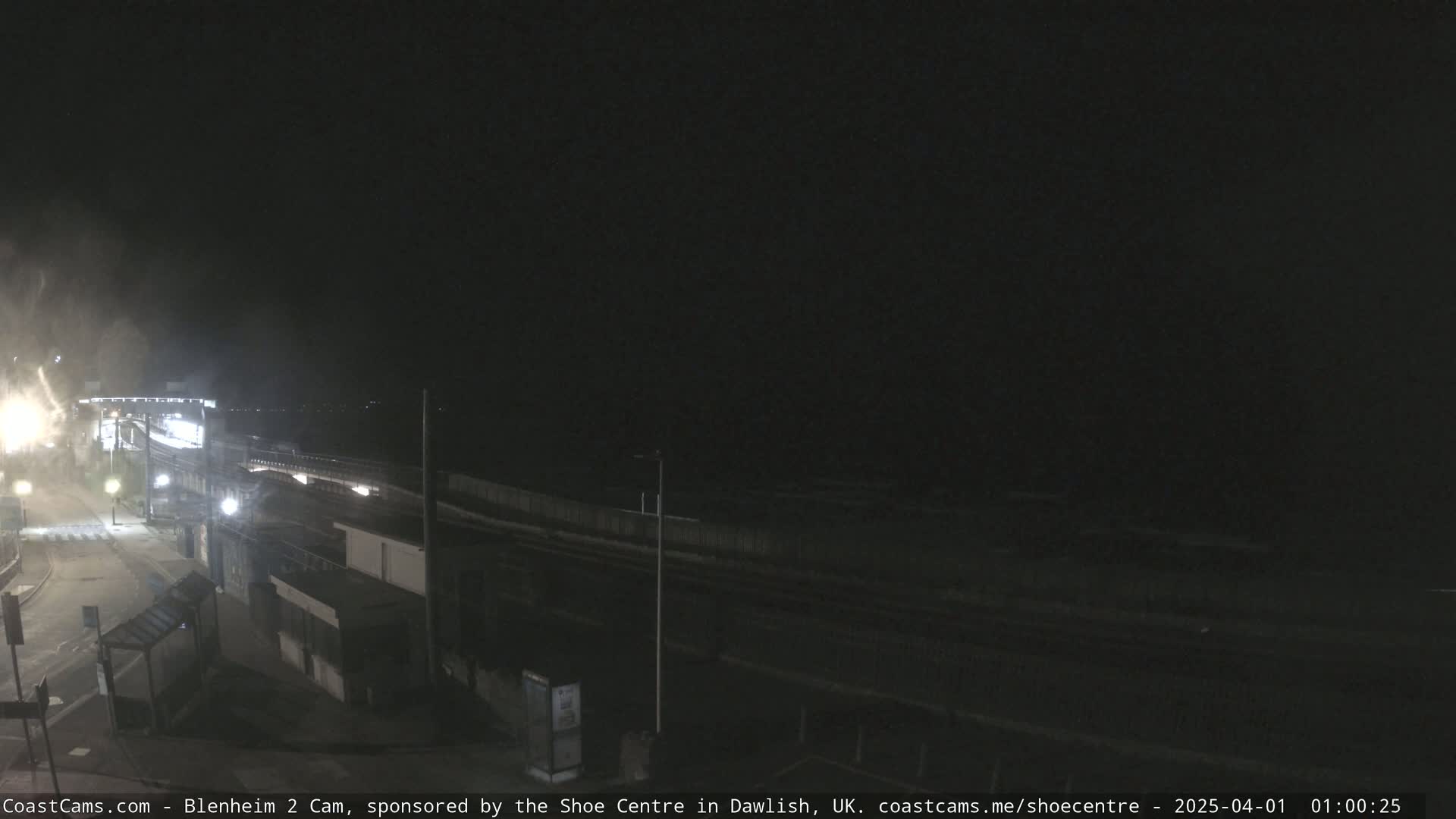 A nighttime view of a coastal road and buildings, with dark, overcast conditions.