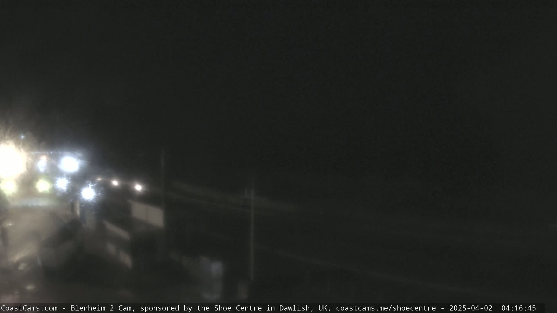 A nighttime, blurry view of a road with headlights visible in the distance, possibly in rainy conditions.