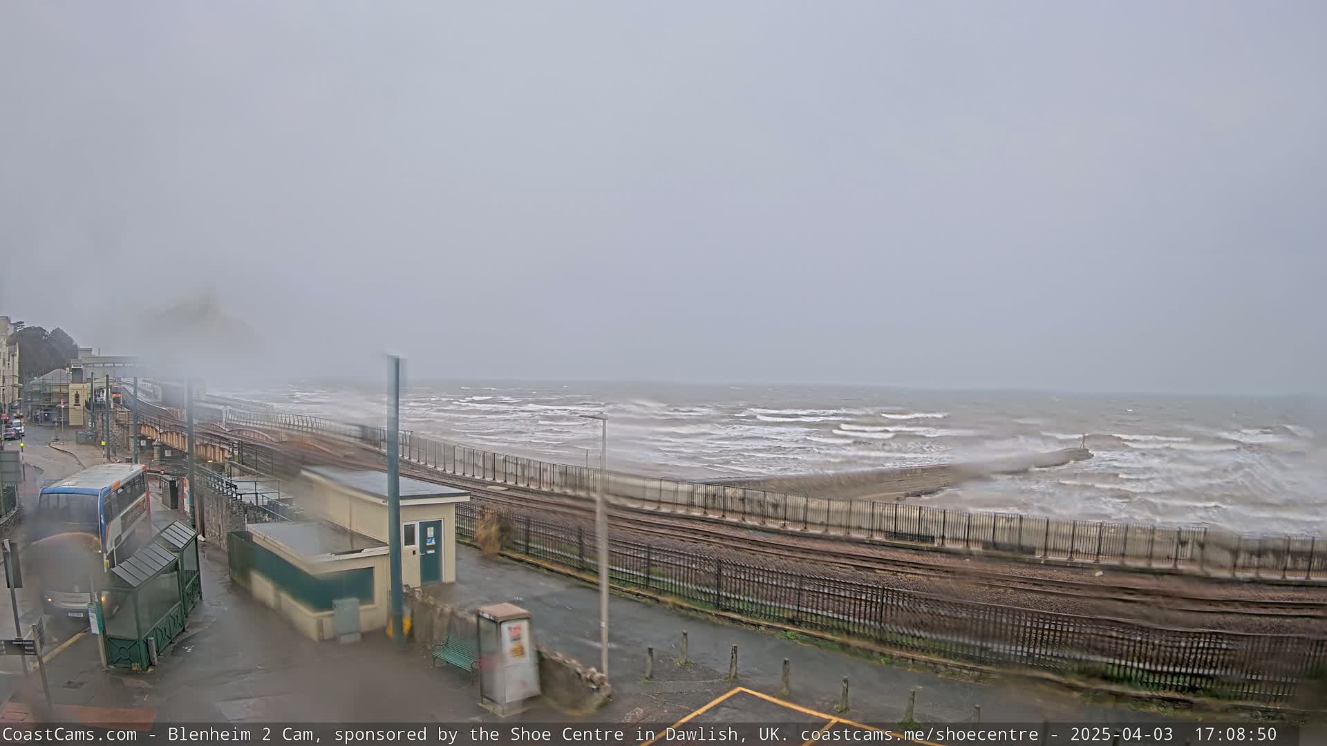 A seaside train track runs alongside a turbulent ocean under an overcast sky.