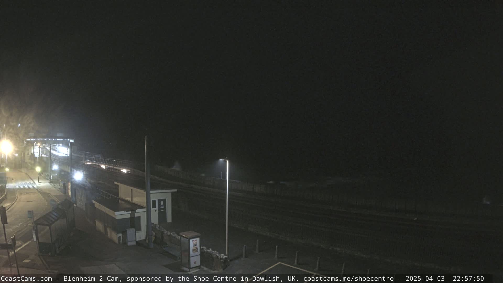 A nighttime view of a seaside train station with dark, choppy water visible in the background.
