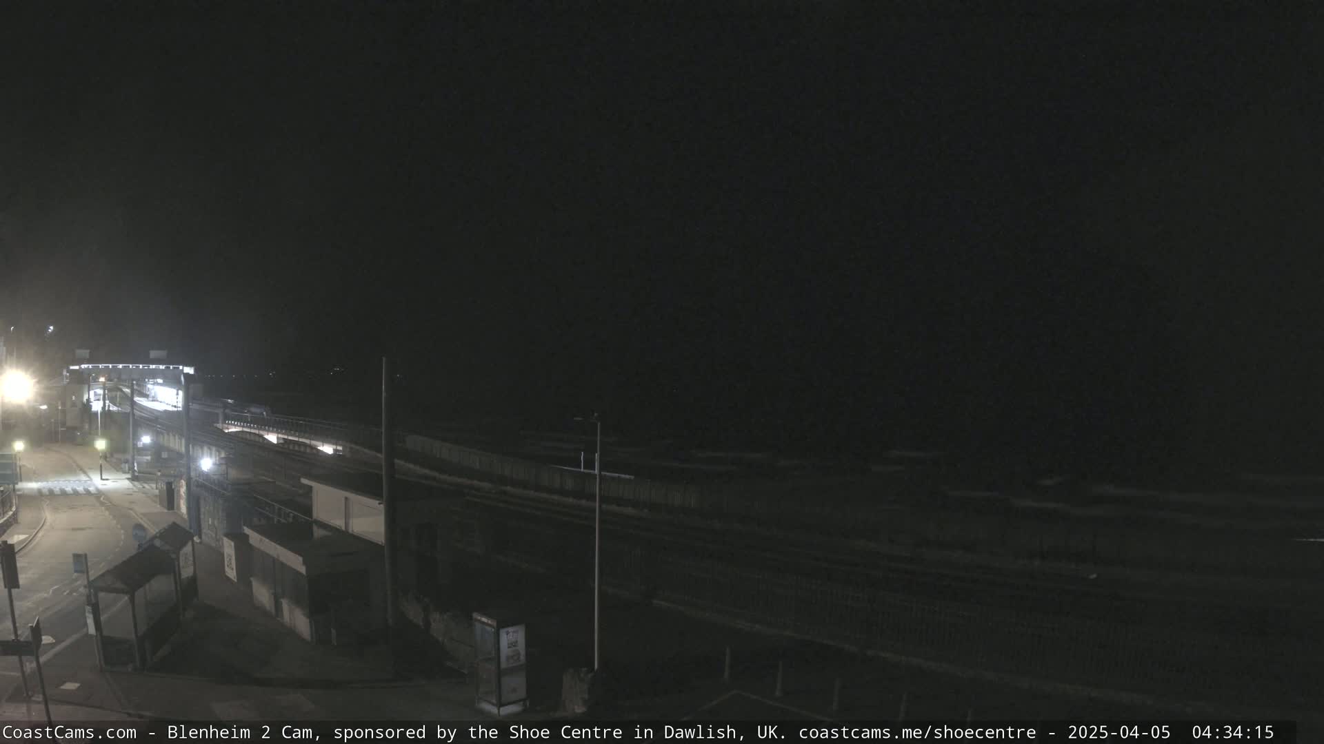 A nighttime view of a train station and coastline, under a dark sky.