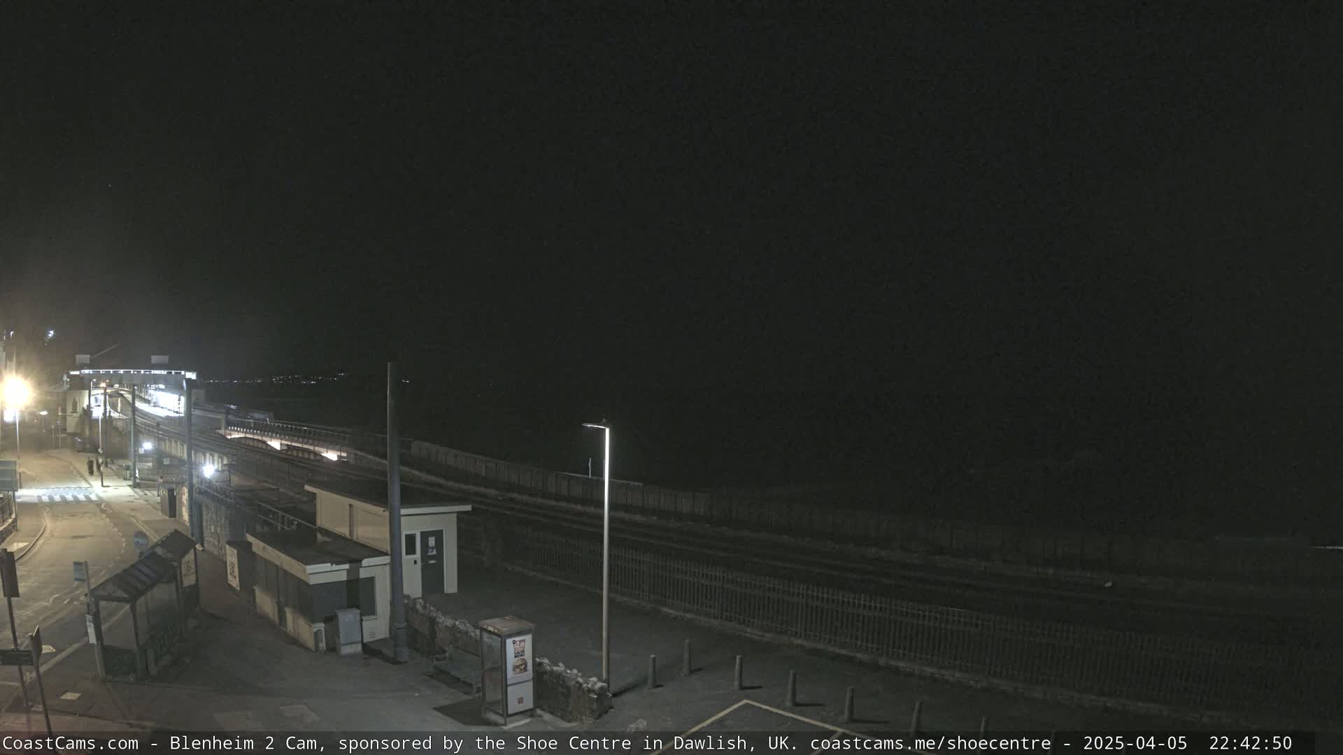 A nighttime view of a train station platform and surrounding area, under a dark, clear sky.