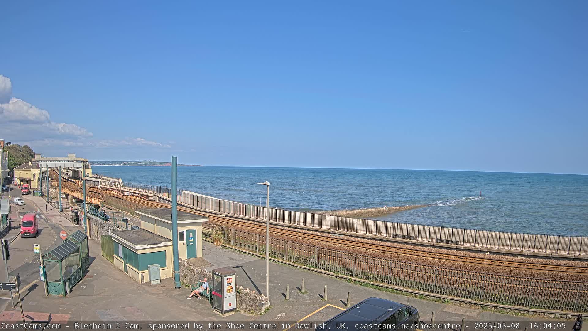 A seaside train track curves alongside a calm ocean under a clear blue sky.