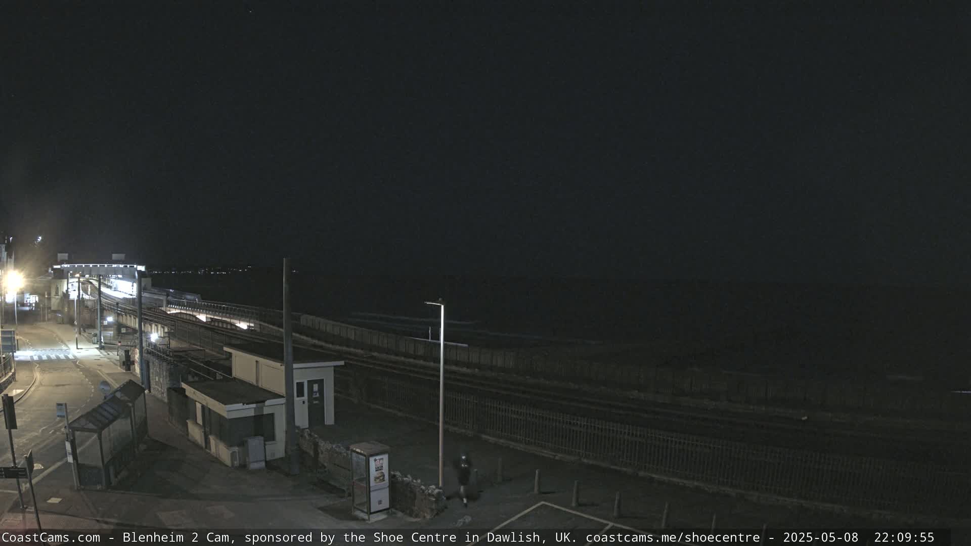 A nighttime view of a train station near the ocean, with calm water visible in the distance under a dark sky.