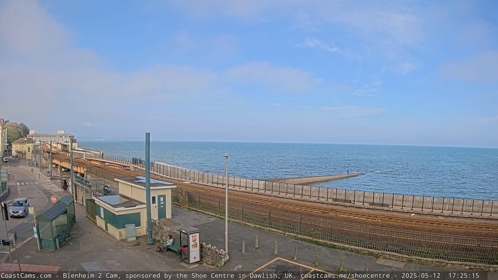 A seaside train station with a calm ocean under a mostly clear sky.