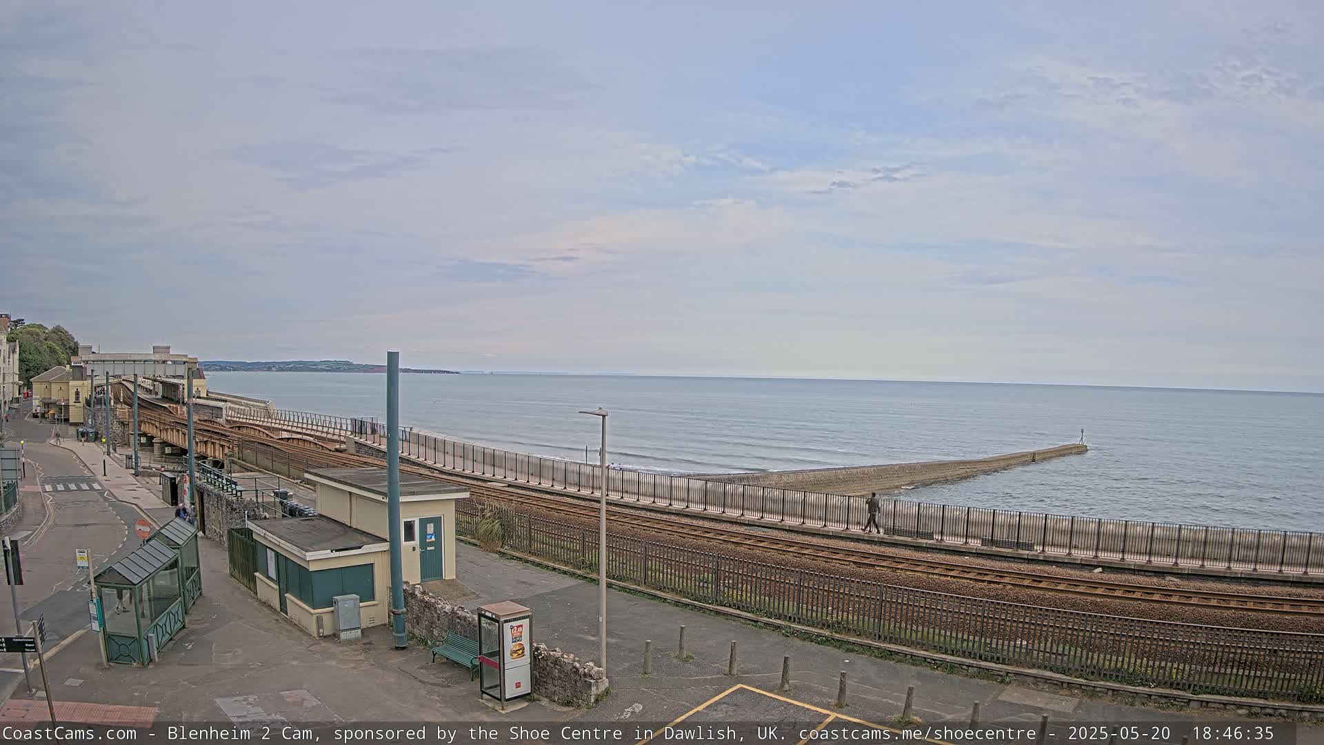 A coastal railway line runs alongside a beach with a calm sea under a mostly cloudy sky.