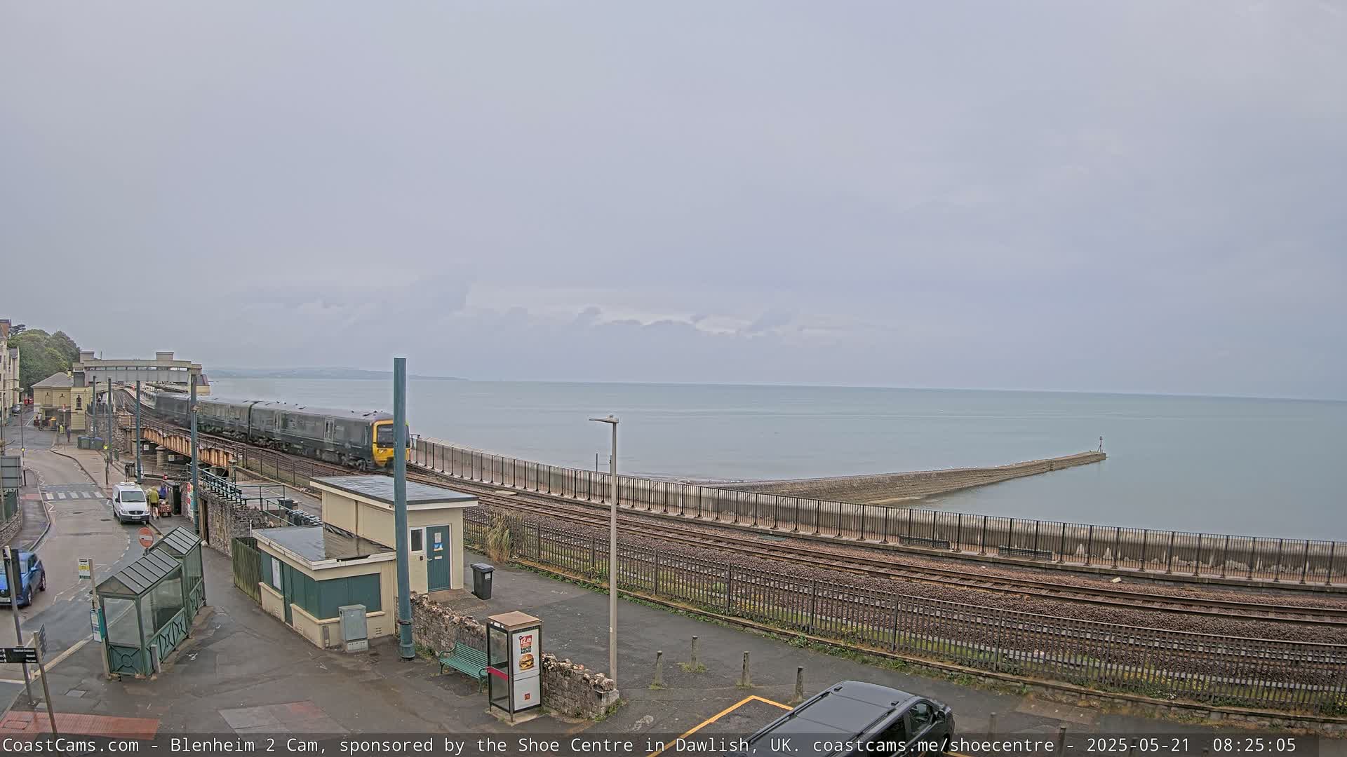 A train passes by a seaside train station on an overcast day.