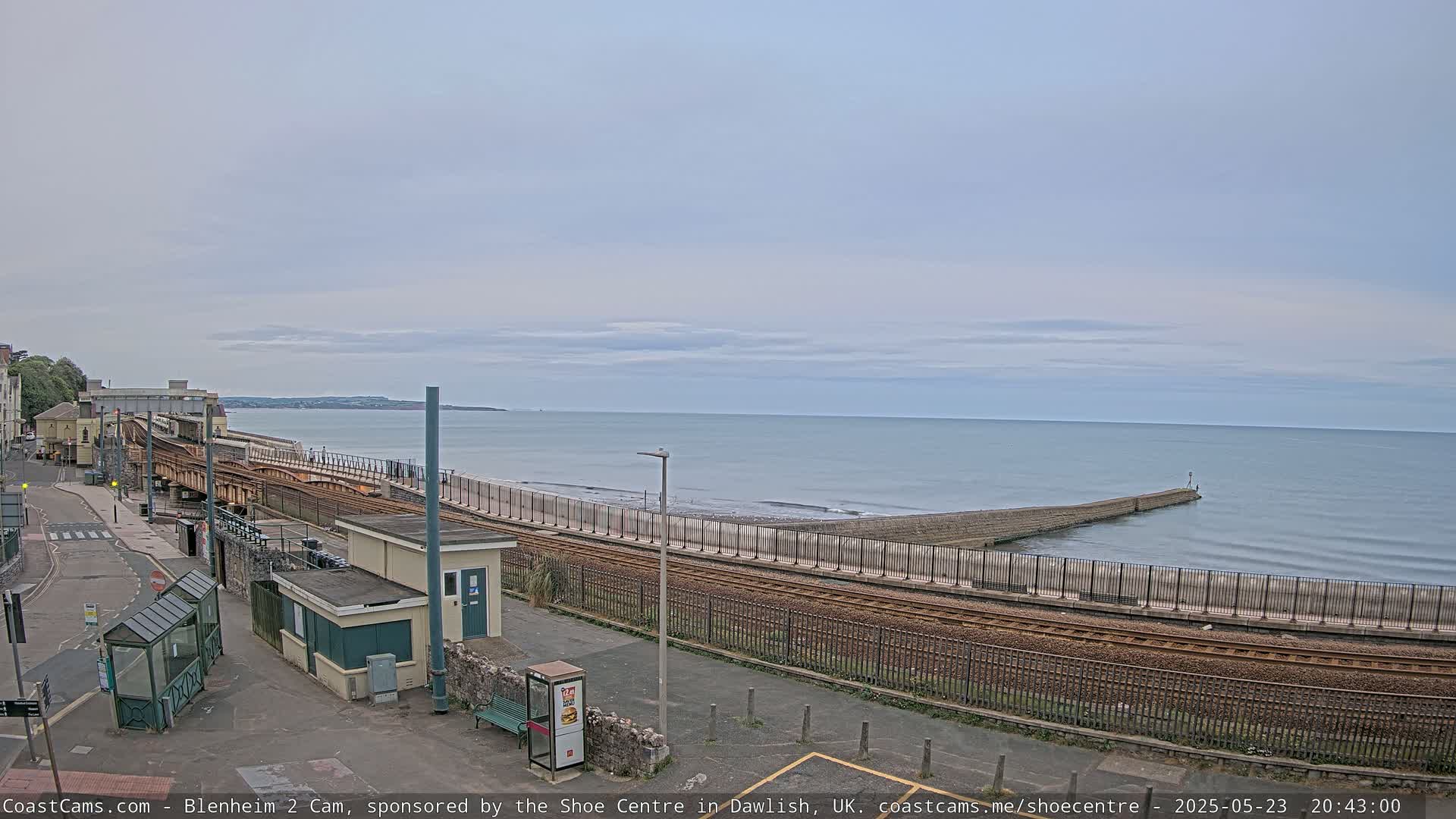 A coastal train track runs alongside a beach and a calm sea under a cloudy sky.