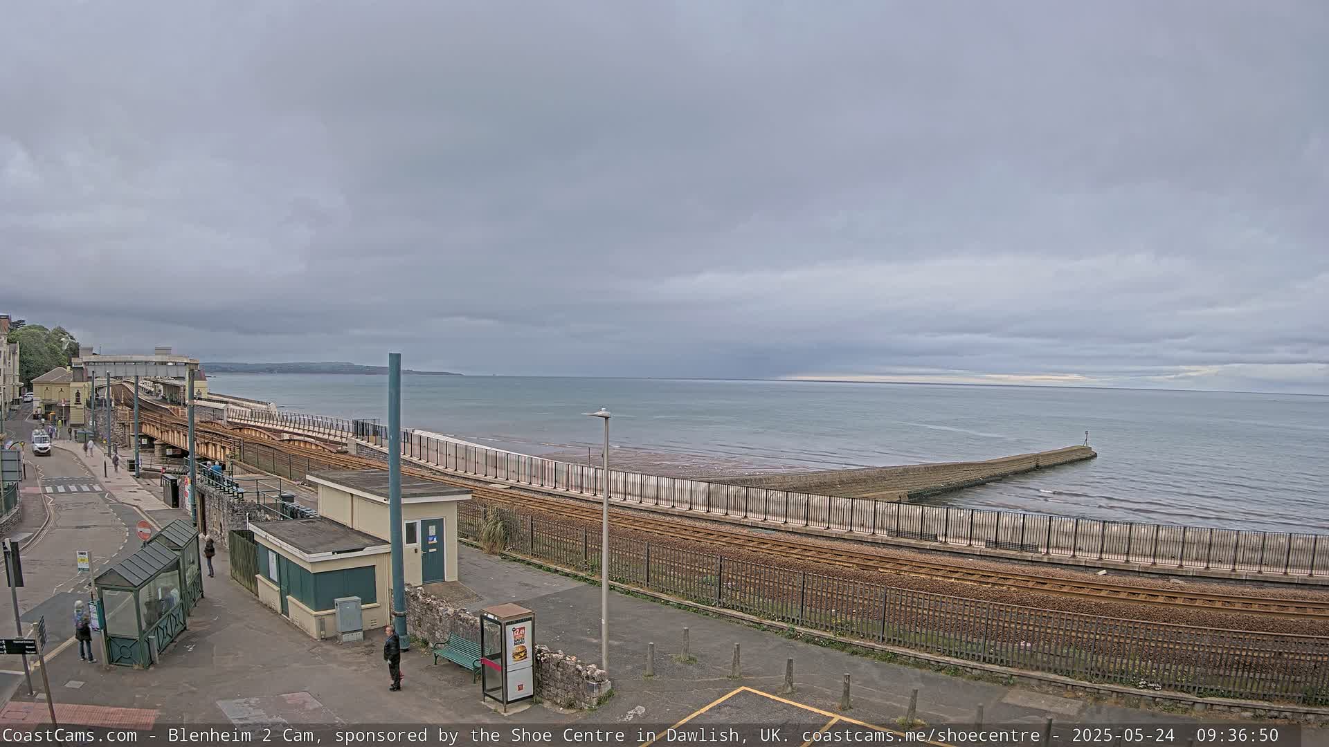 A coastal railway line runs alongside a calm sea under an overcast sky.