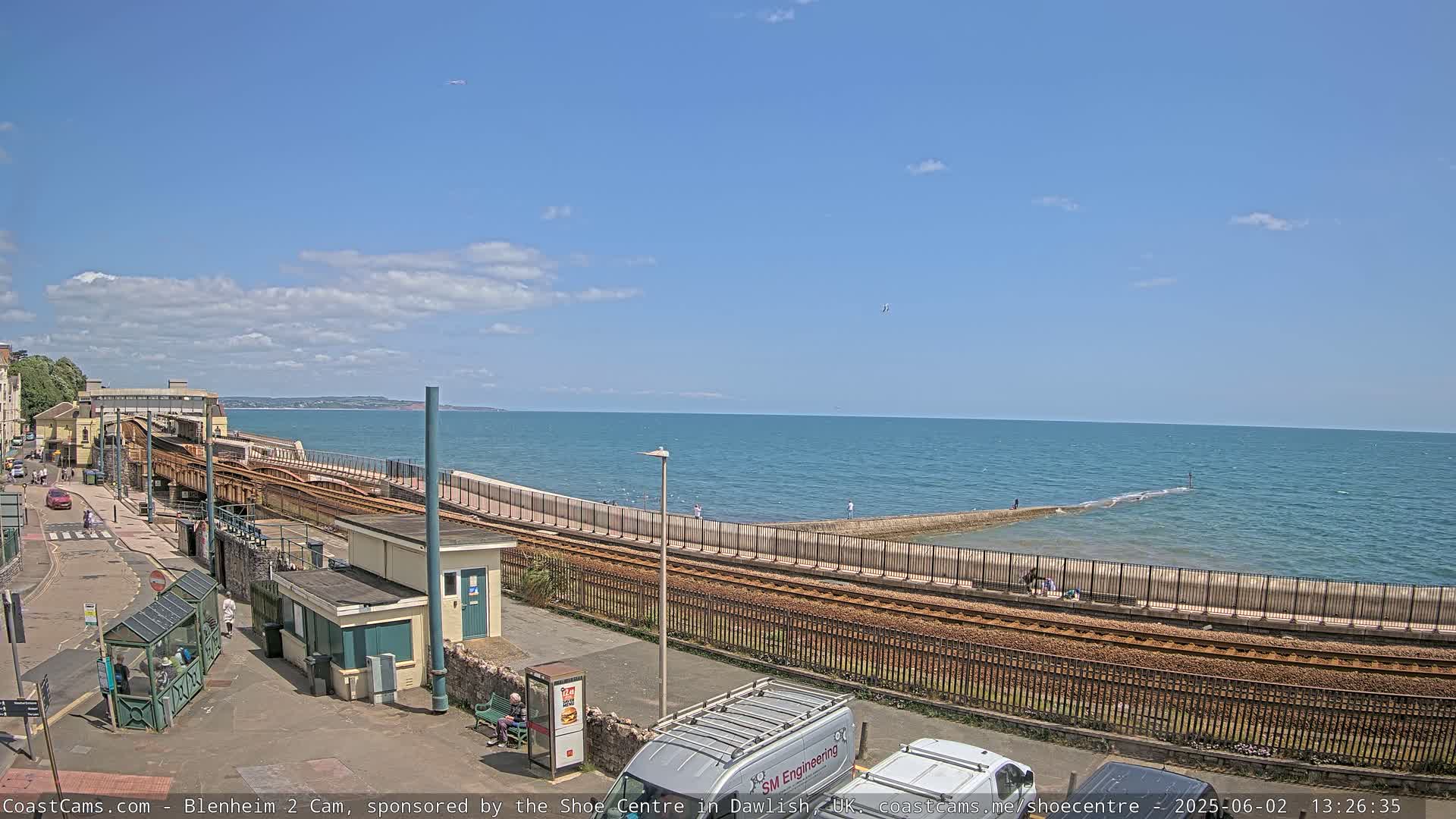 A sunny day overlooking a seaside town with train tracks running alongside a sea wall and calm ocean waters.