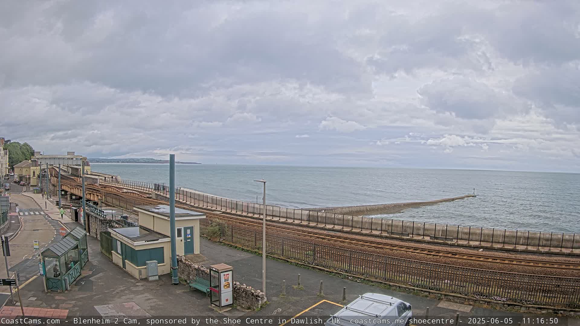 A coastal railway line runs alongside a sea wall, overlooking a choppy sea under a cloudy sky.