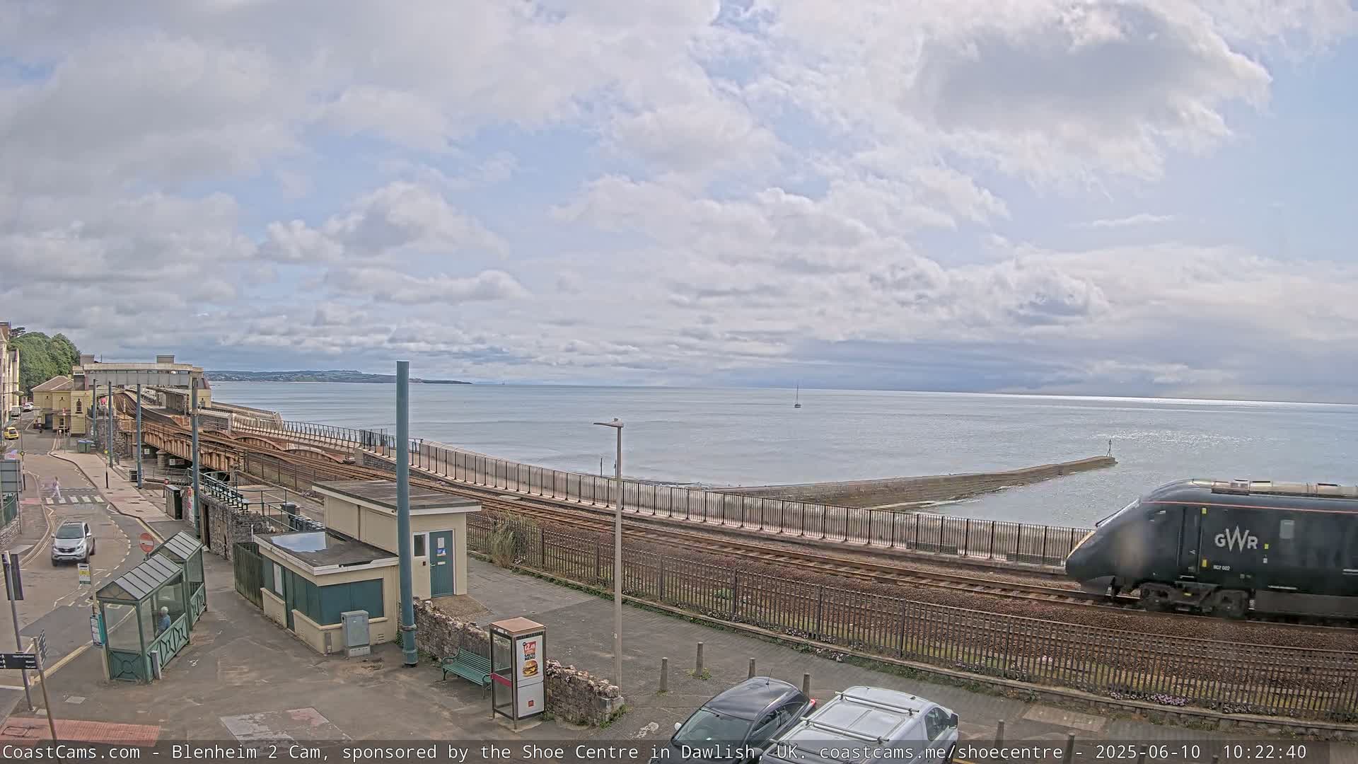 A black train passes by a seaside railway line under a partly cloudy sky.