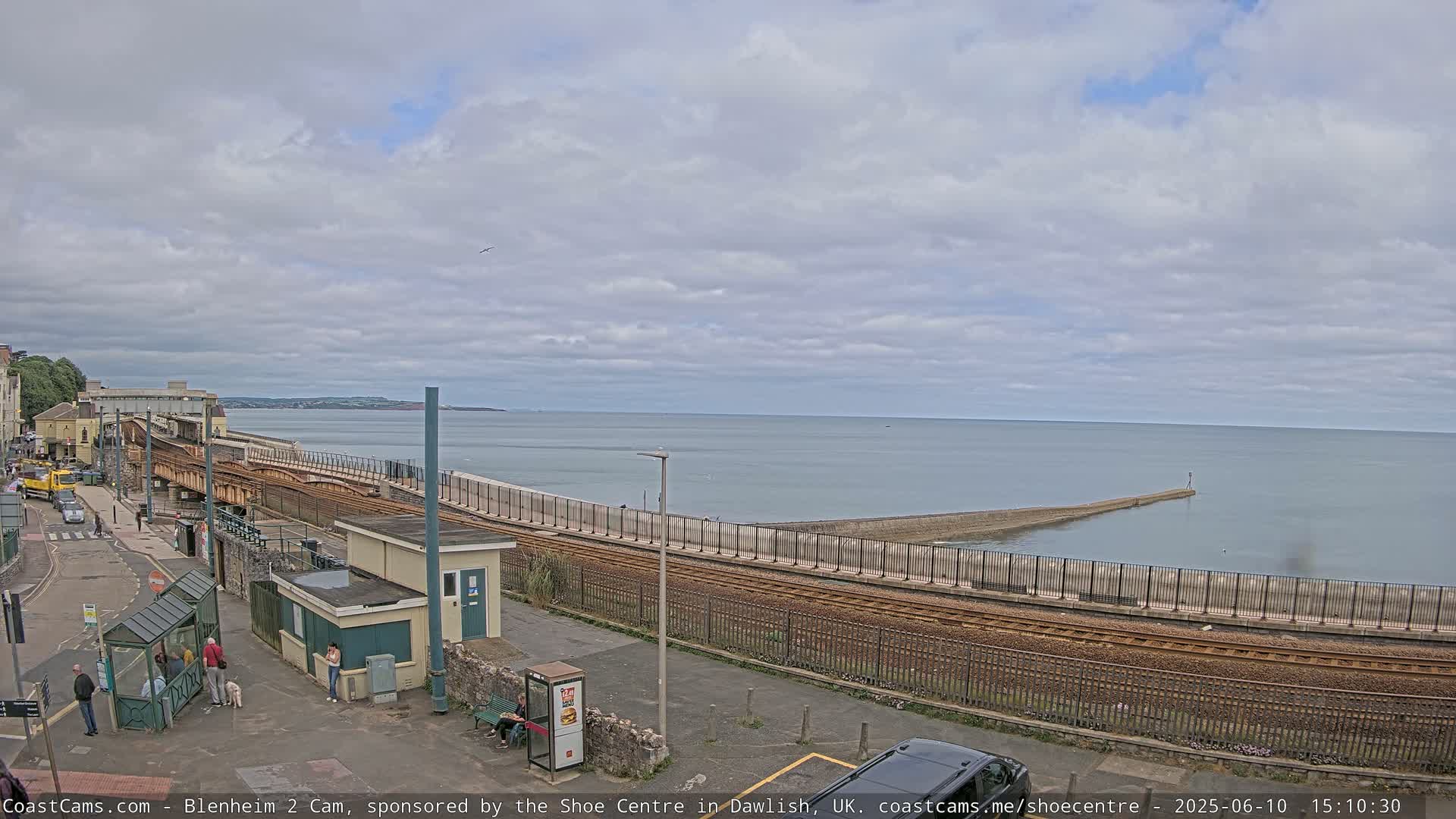 A coastal railway line runs alongside a sea wall, with a calm sea and overcast sky in the background.