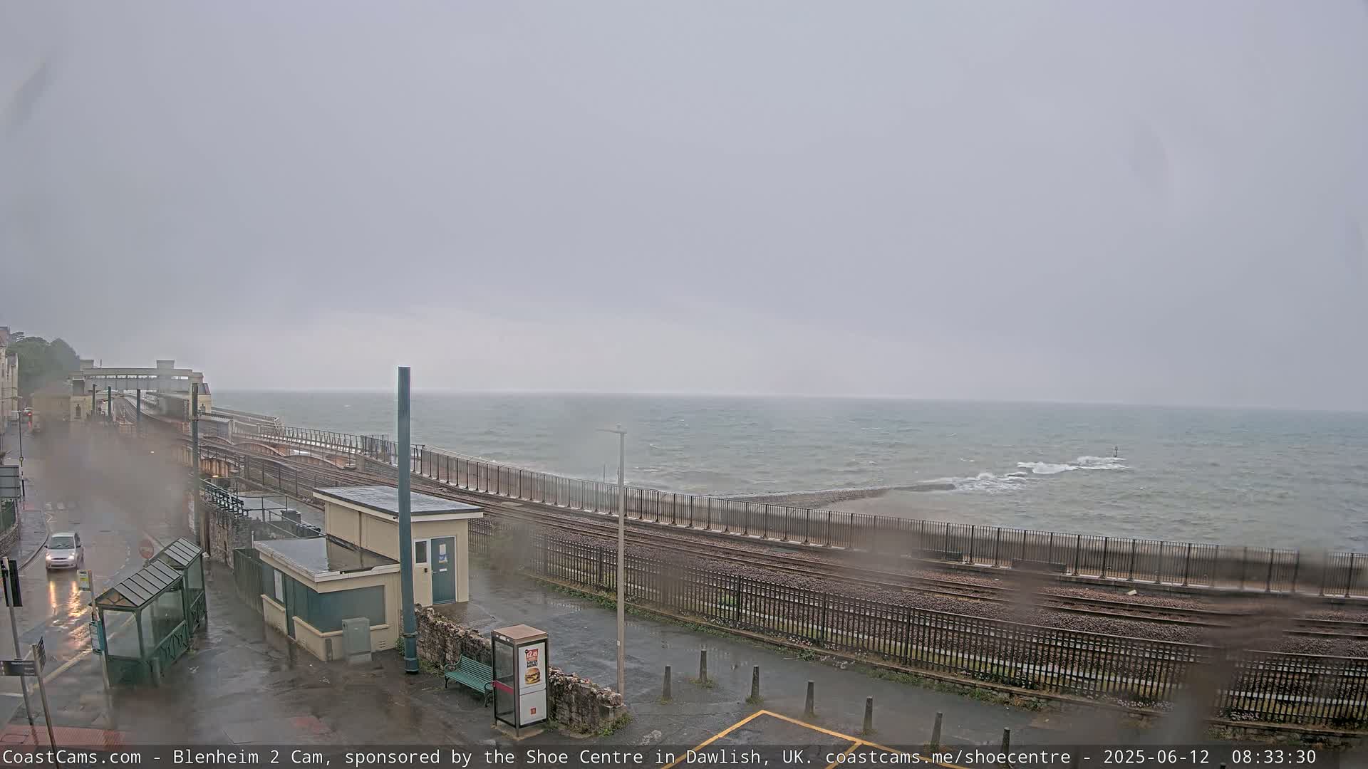 A rain-soaked railway station overlooks a choppy sea under a gray sky.