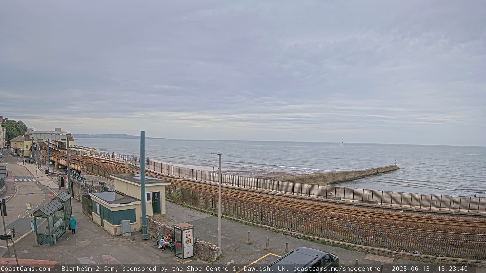 A train track runs alongside a beach and ocean under an overcast sky.