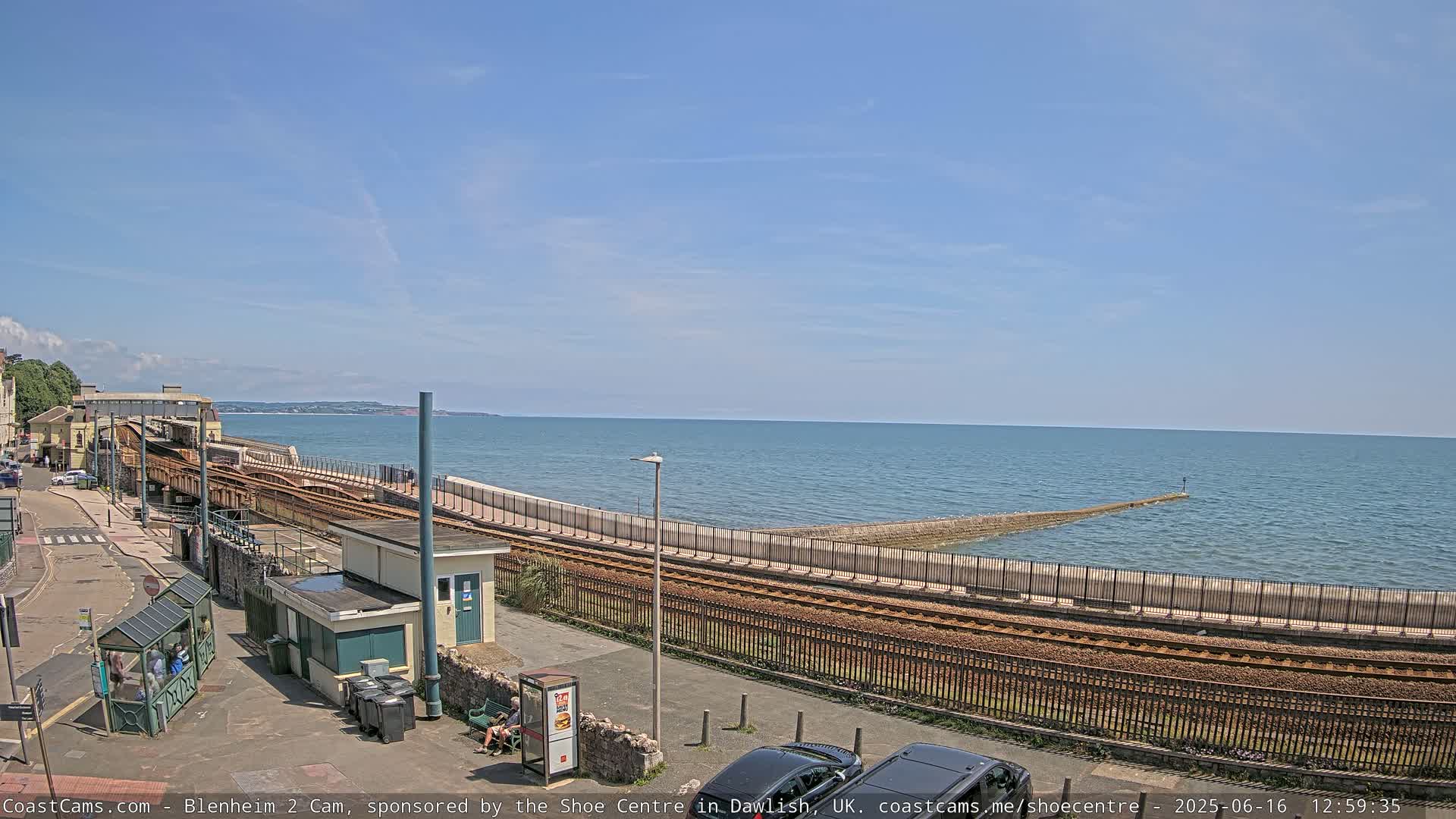A seaside train track runs alongside a calm ocean under a clear blue sky.