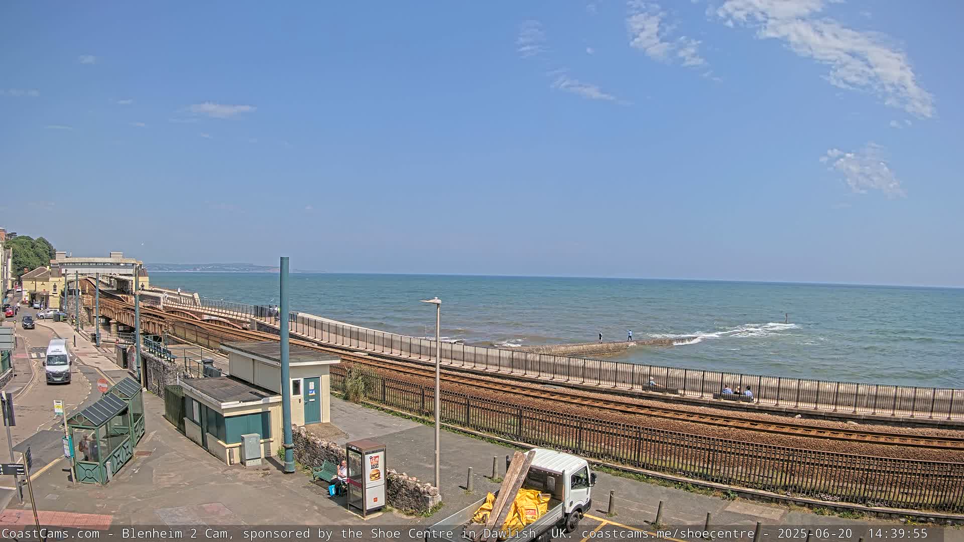 A seaside train track curves along a coastline on a sunny day with a calm sea.