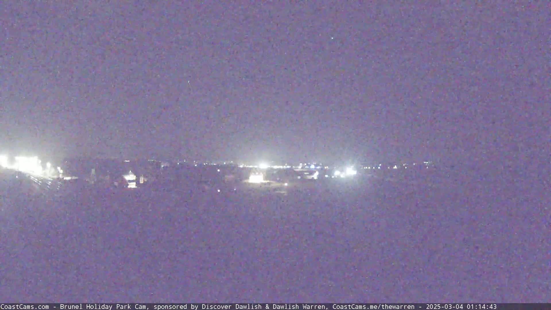 A nighttime long shot shows a dimly lit town under a dark, clear sky.