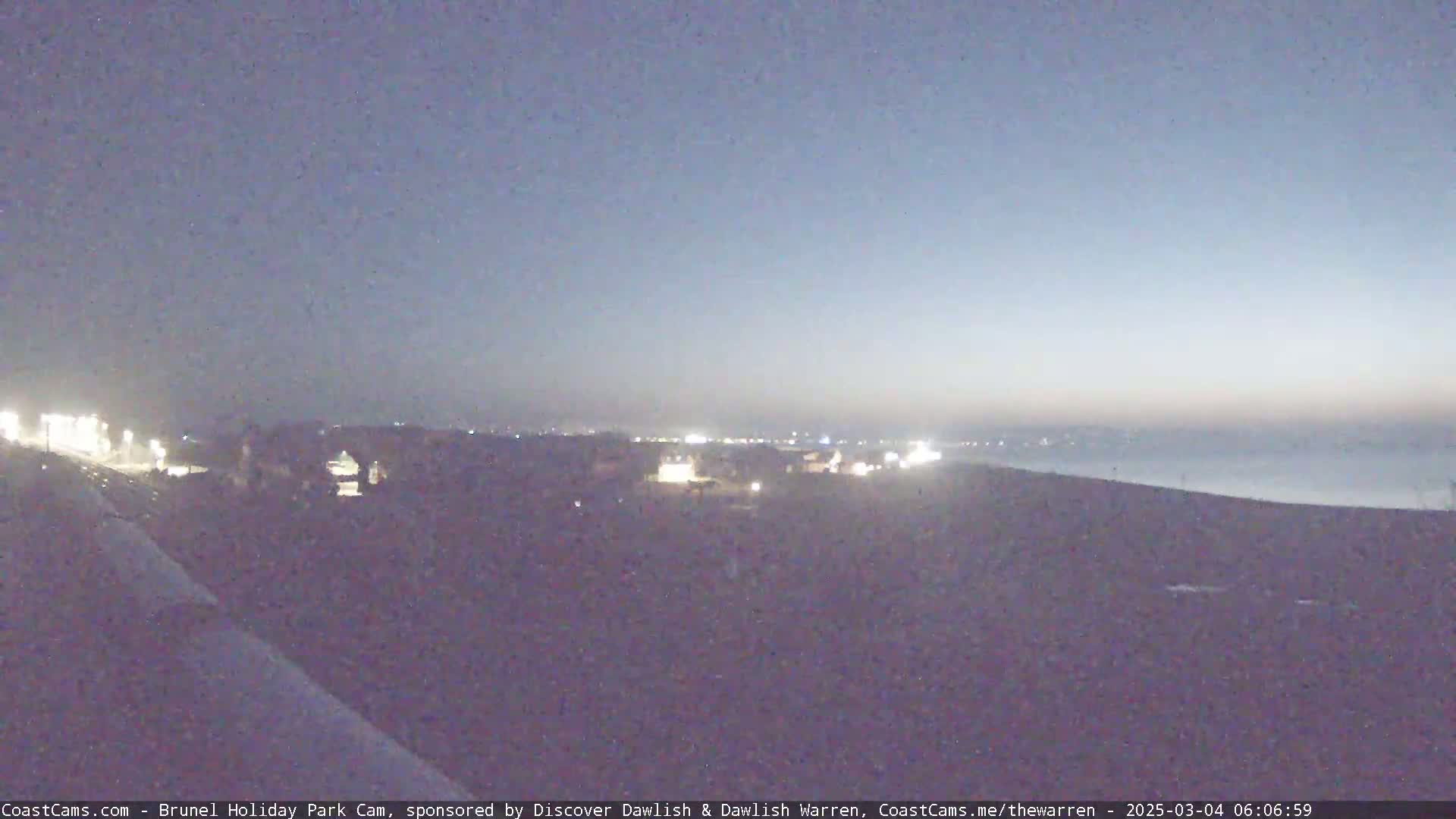 A dimly lit coastal town is visible at twilight under a clear, dusky sky.