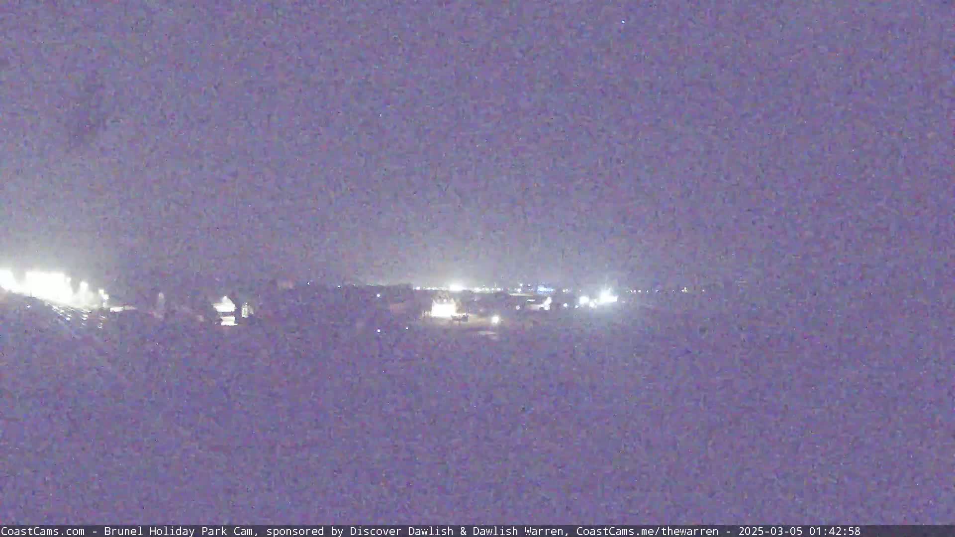 A nighttime, low-light view of a town's outskirts with distant lights visible under a dark sky.