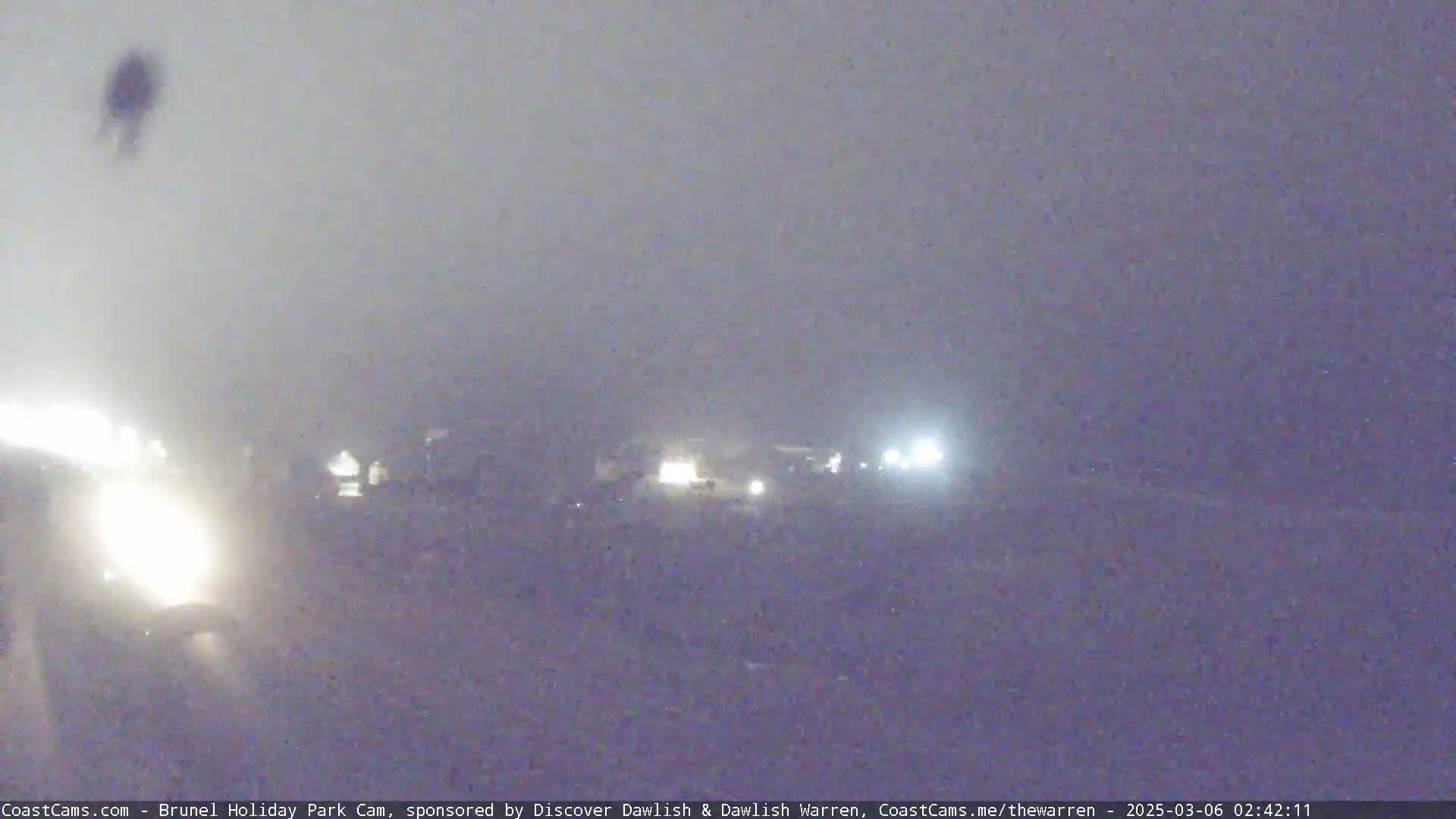 A hazy night scene shows blurry headlights of vehicles on a road.