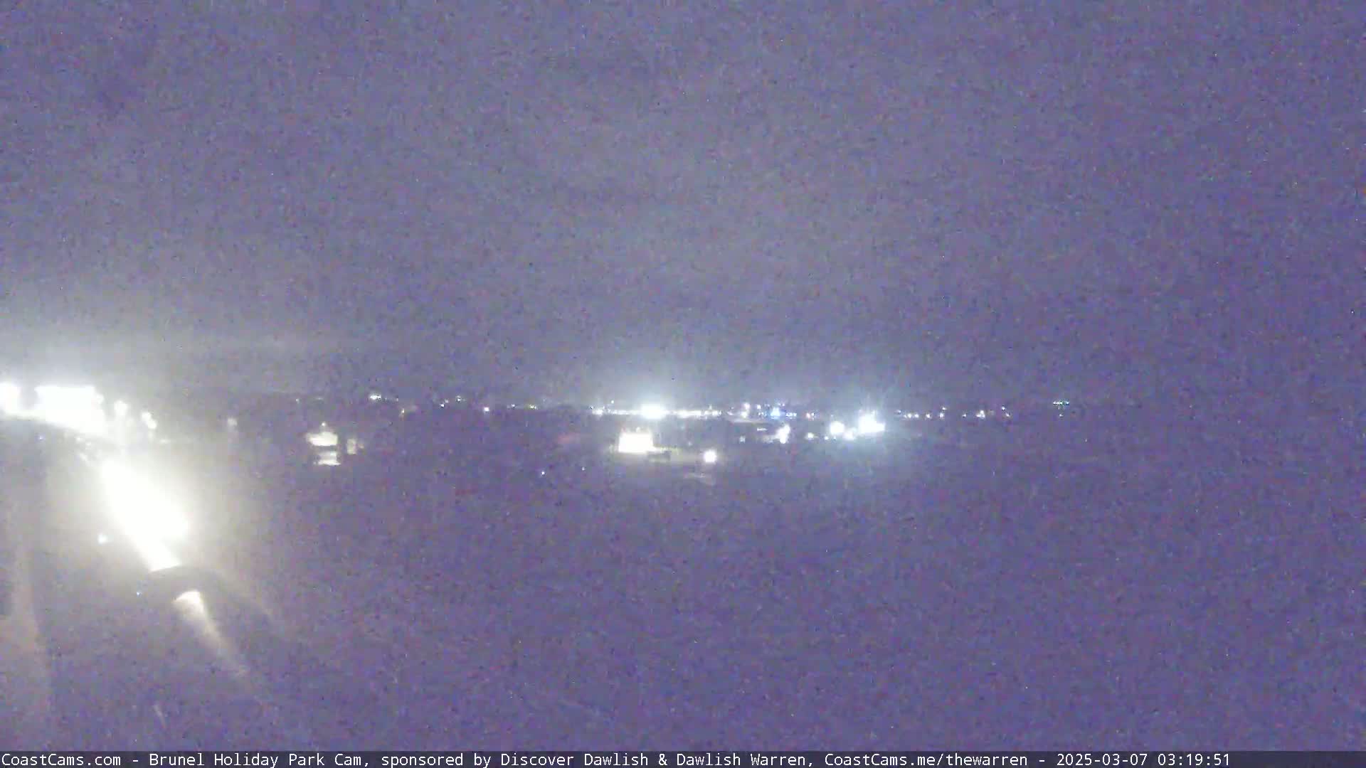 A nighttime long shot shows a distant town's lights under a dark, cloudy sky.