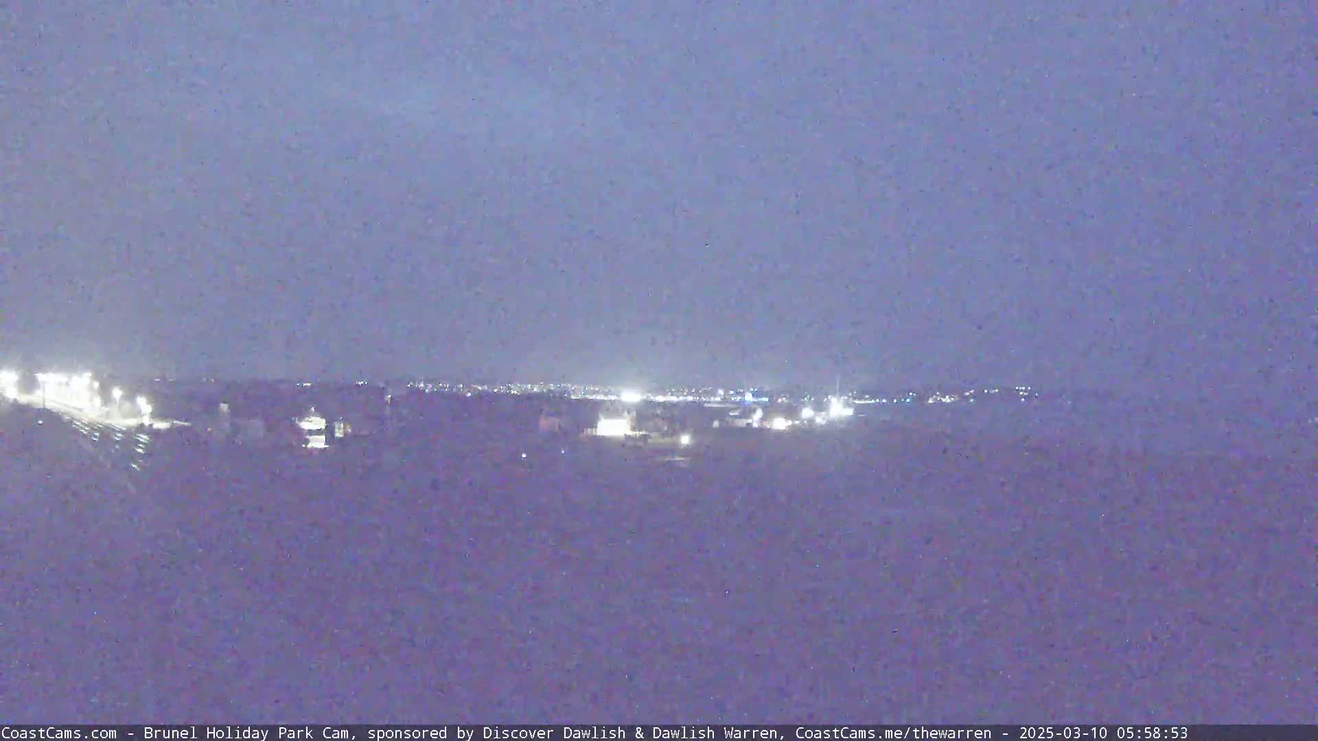 A nighttime long shot shows a distant town's lights under a dark, clear sky.