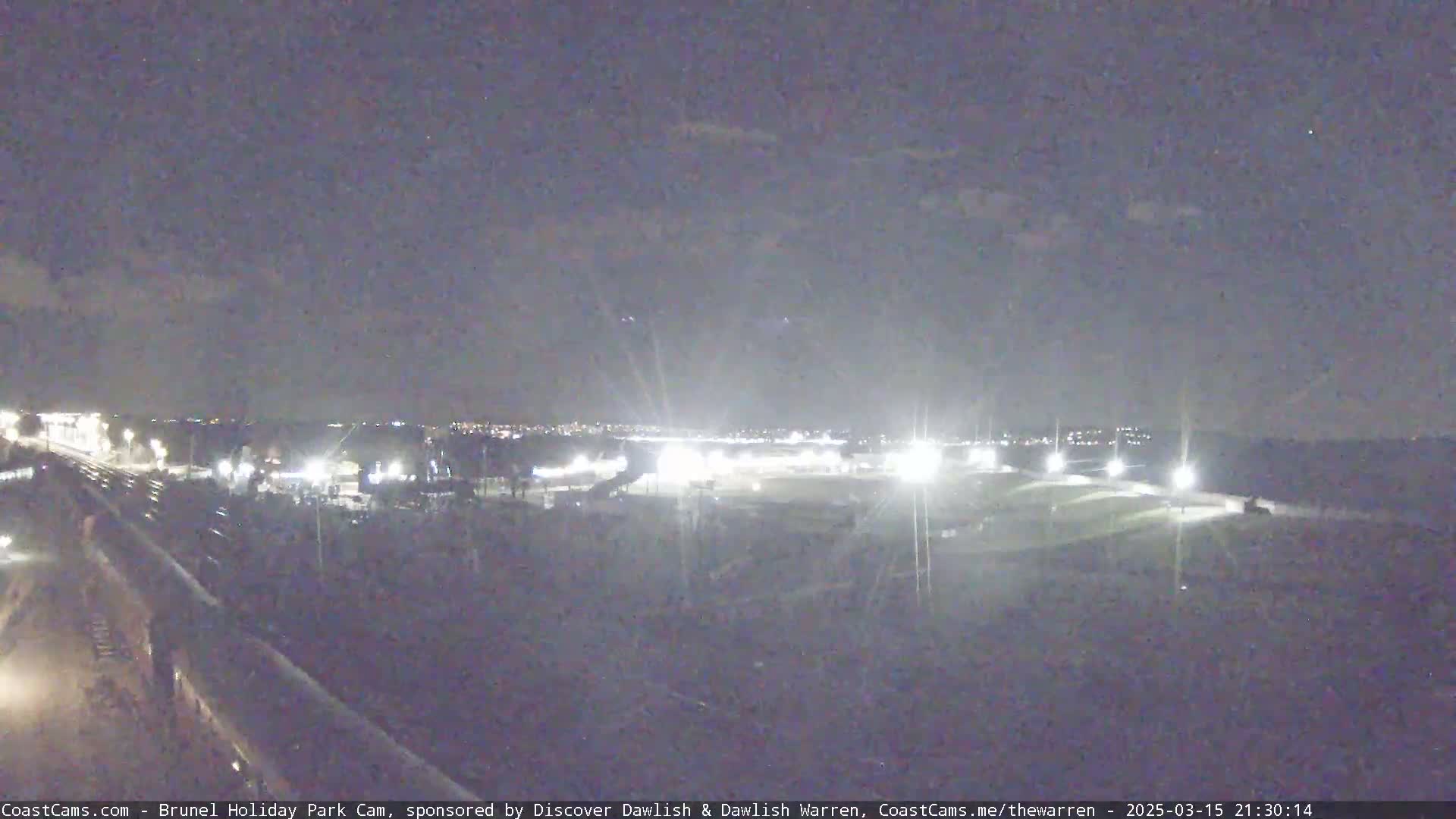 A nighttime view of a dimly lit park and surrounding area, under a dark, overcast sky.