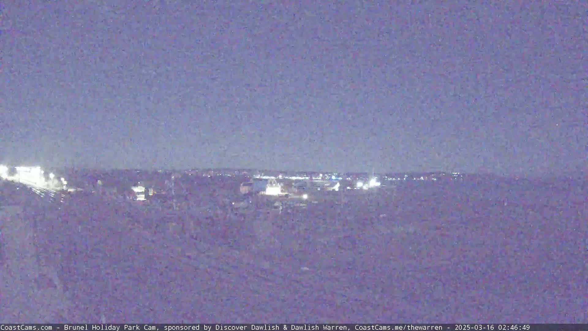 A nighttime long shot shows a dimly lit town in the distance under a dark, clear sky.