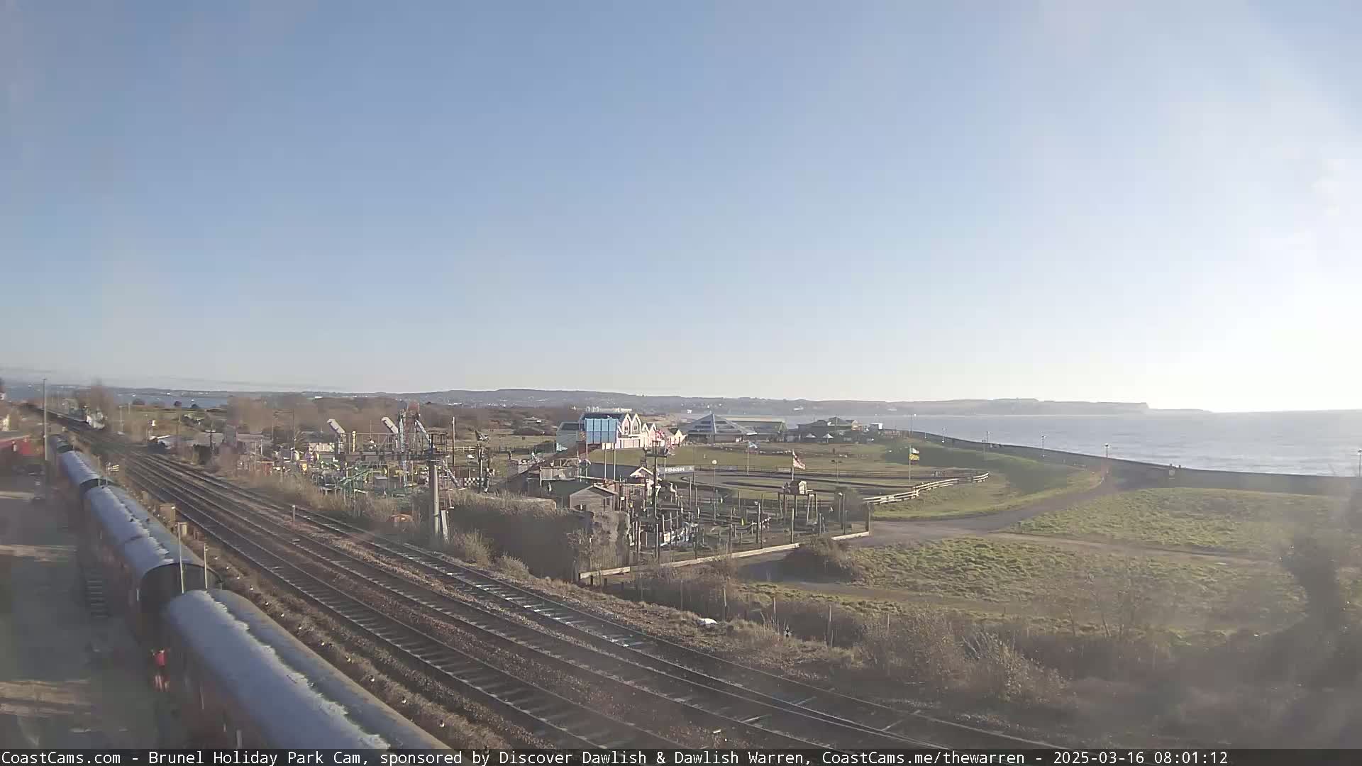 A seaside amusement park with a train track nearby, under a clear blue sky.