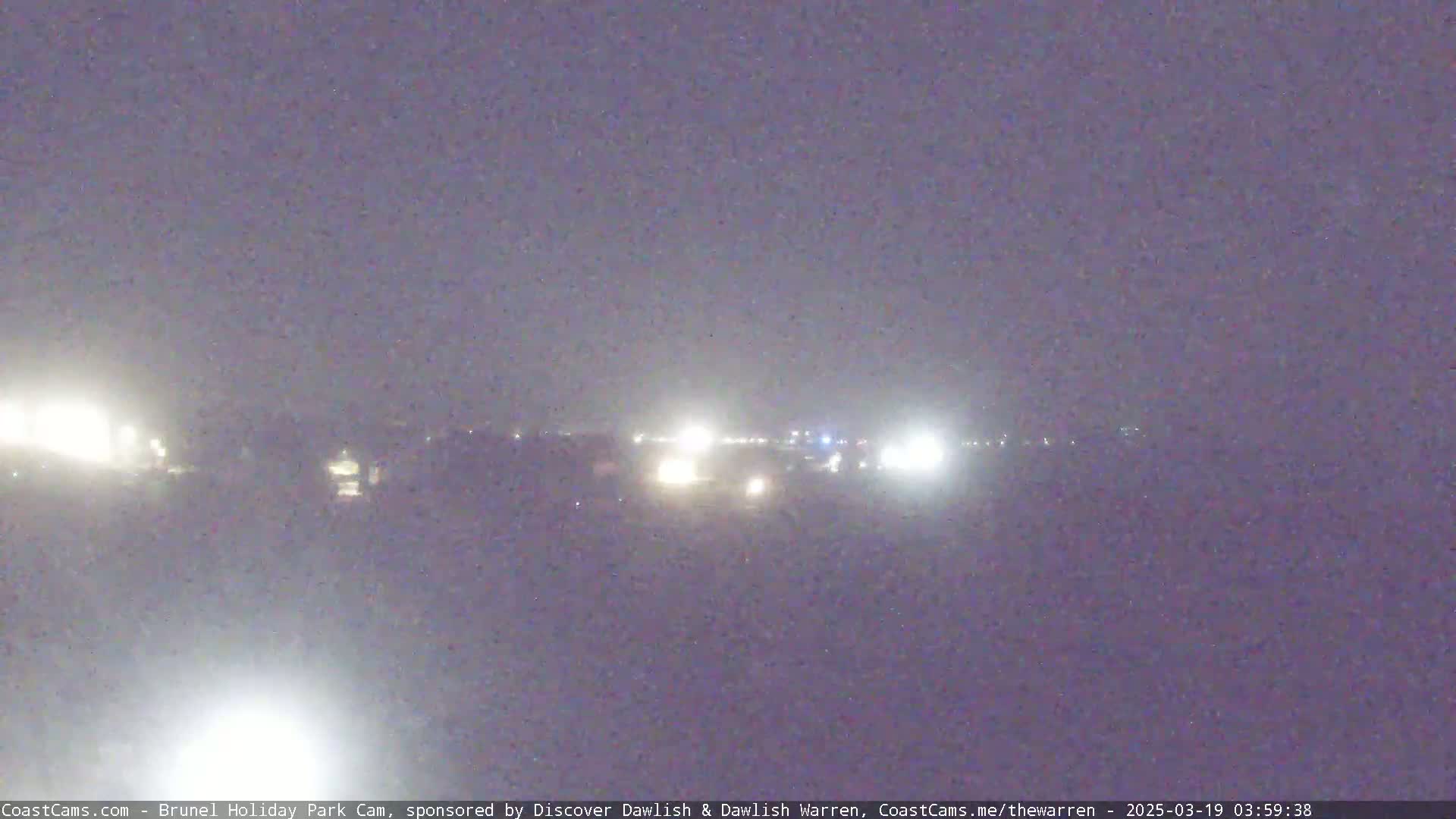 A nighttime, hazy view shows distant headlights on a road.