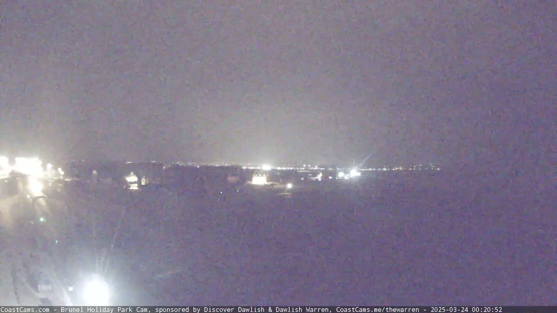 A nighttime long shot shows a dimly lit landscape with a distant city skyline under an overcast sky.
