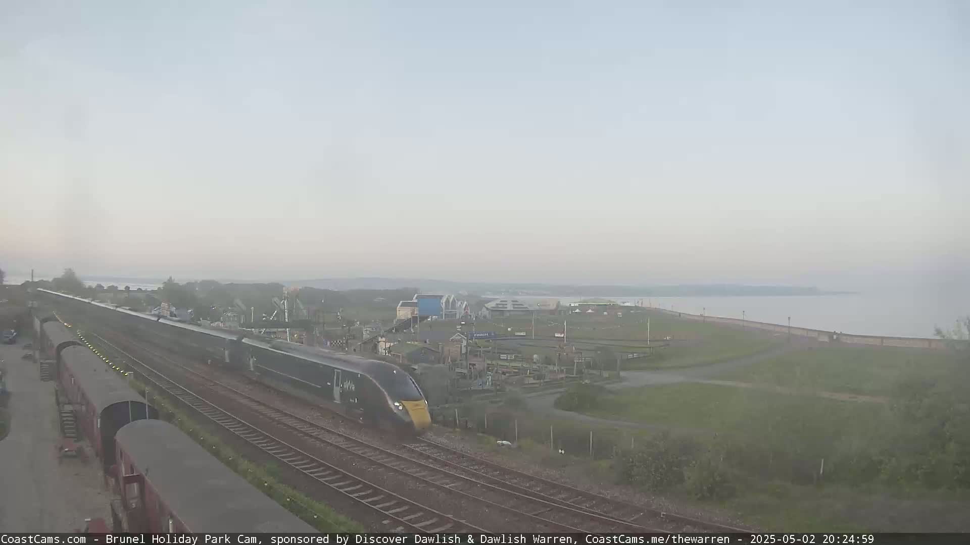 A high-speed train travels along a coastal railway line on an overcast evening.
